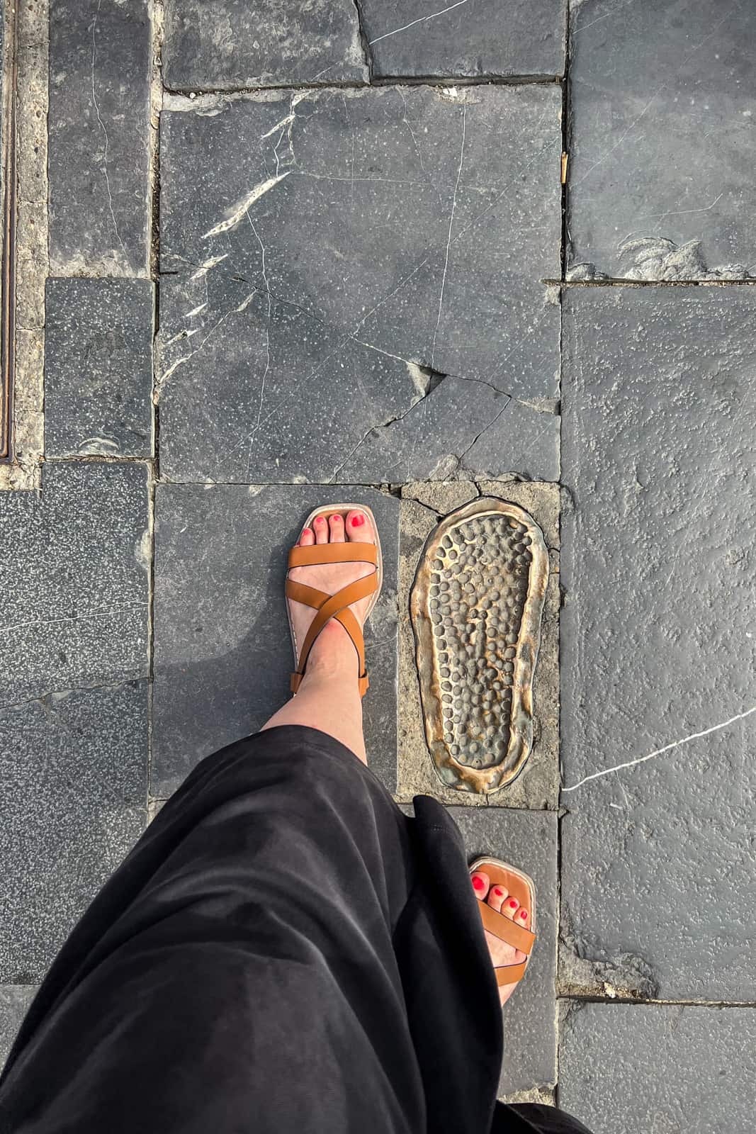 A woman wearing a brown sandal puts her foot next to the bronze footprint of a Roman solider in León. 