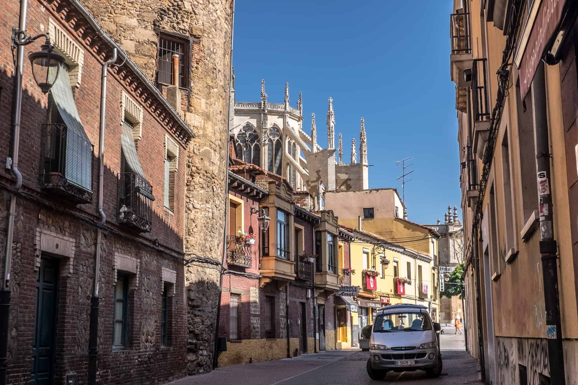 Parts of a Roman stone tower pokes between low rise red brick houses in front of the Cathedral structure in León.