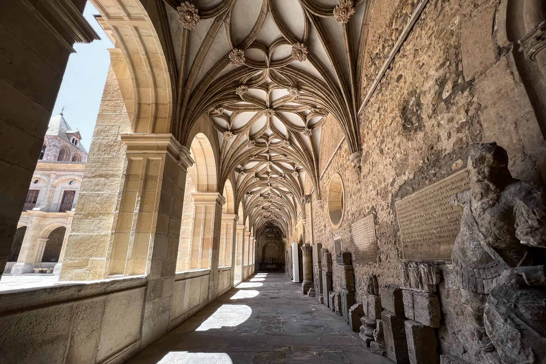 Statues and tombstones line the wall of the golden stone cloister in the Basílica de San Isidoro de León.