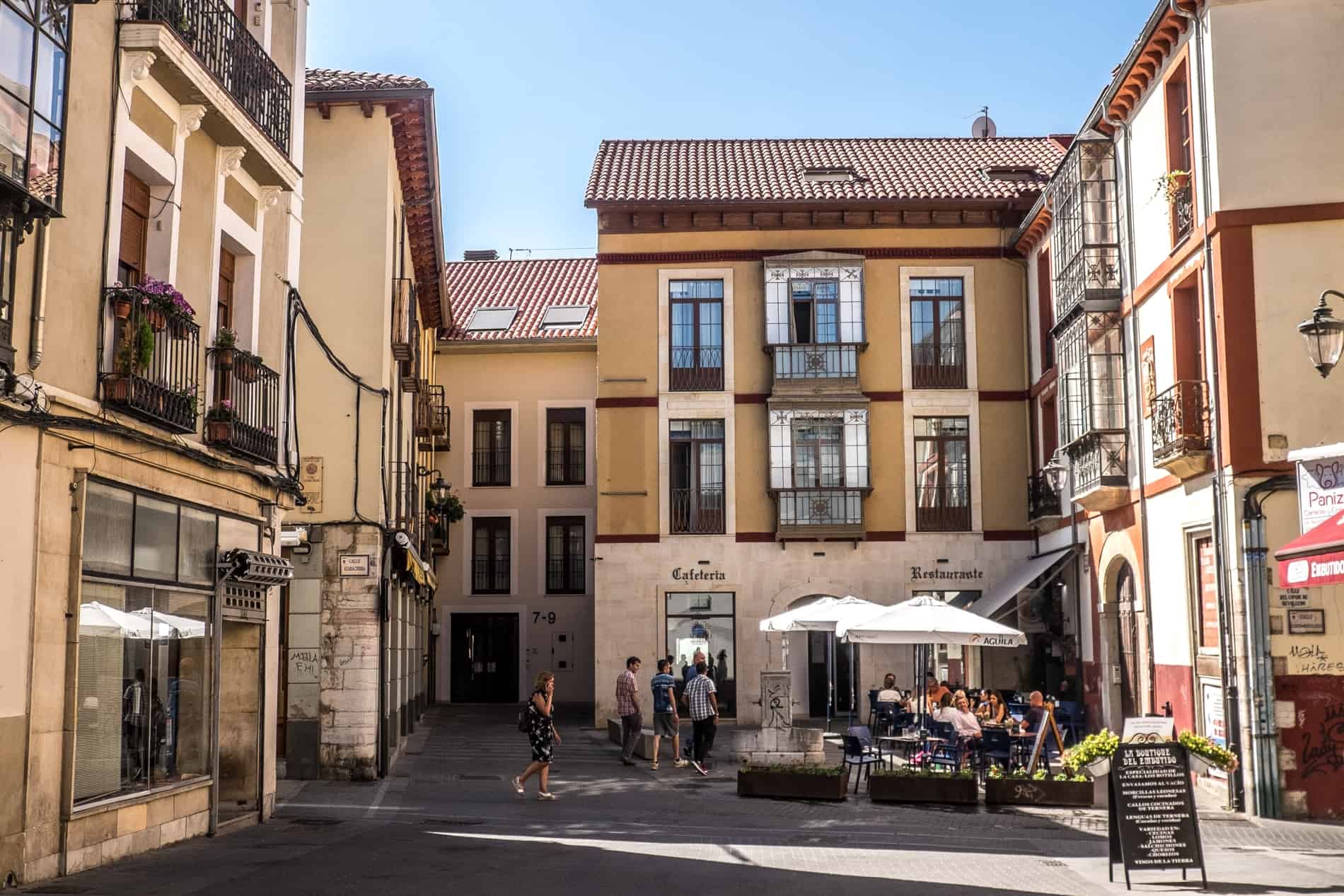 People at a cafe on a small open square surrounded by yellow-painted buildings. 