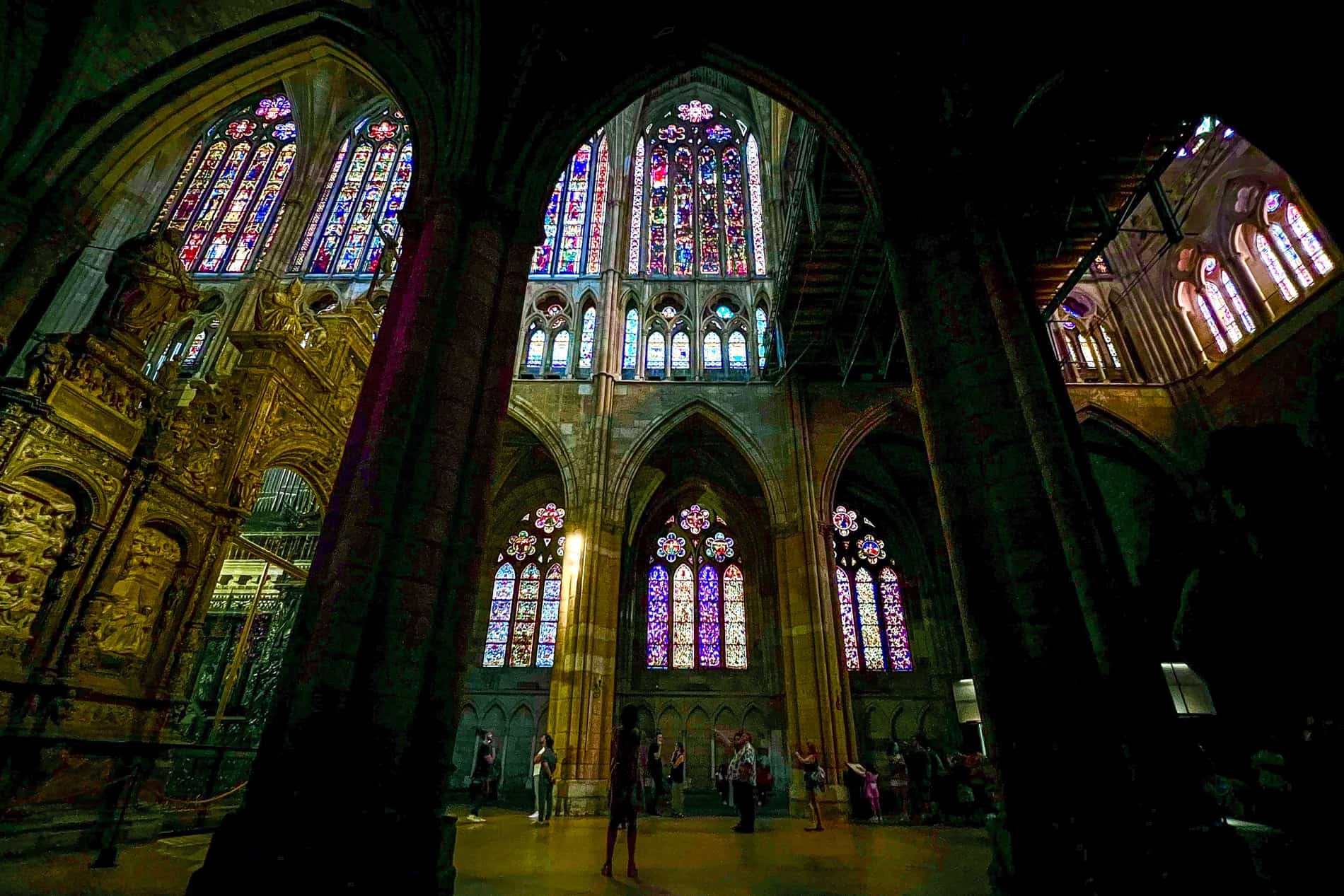 A view from behind an arcade archway of the multicoloured stained glass windows of León Cathedral.