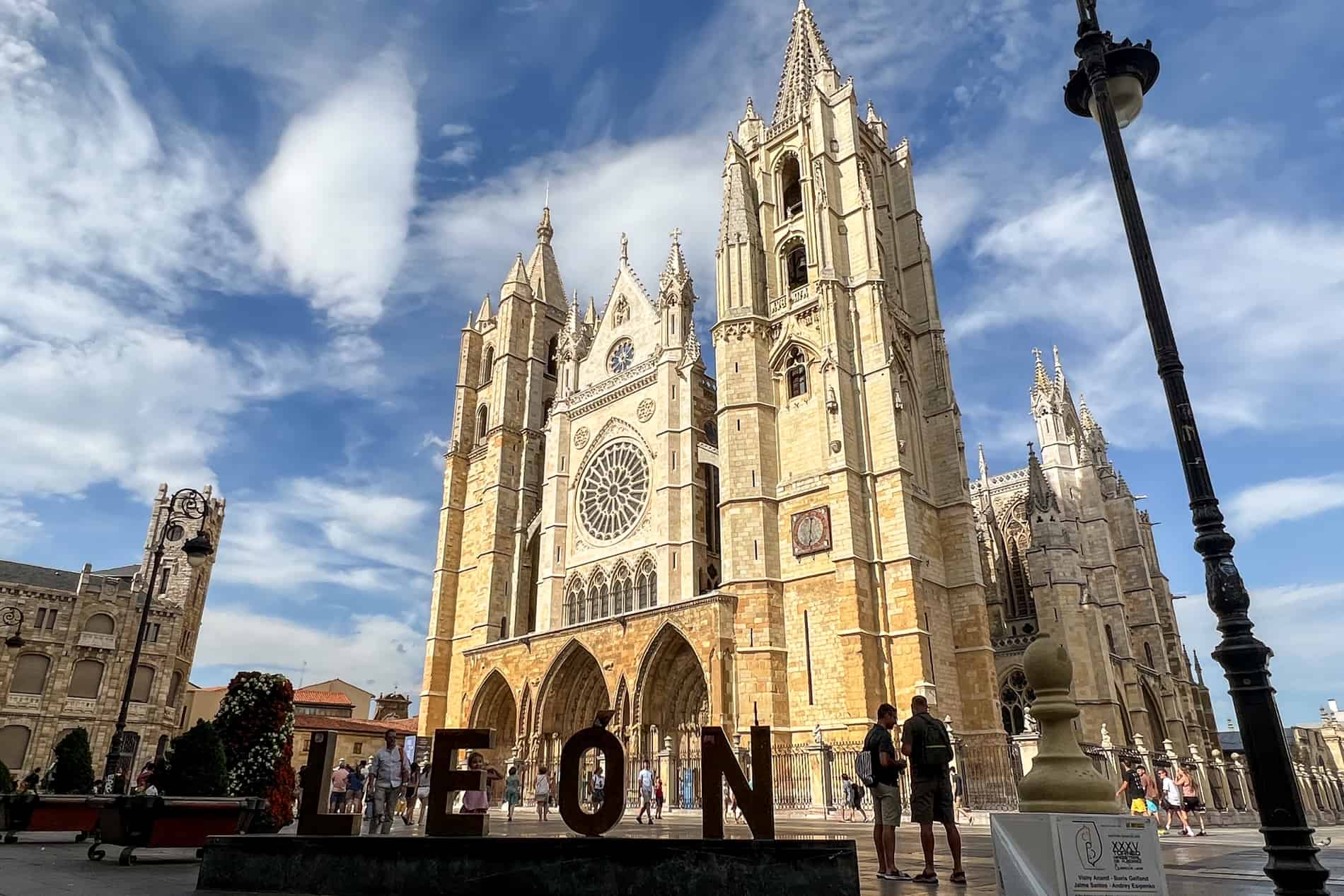 The towering golden gothic structure of Leon Cathedral with a Leon city sign in front of it.