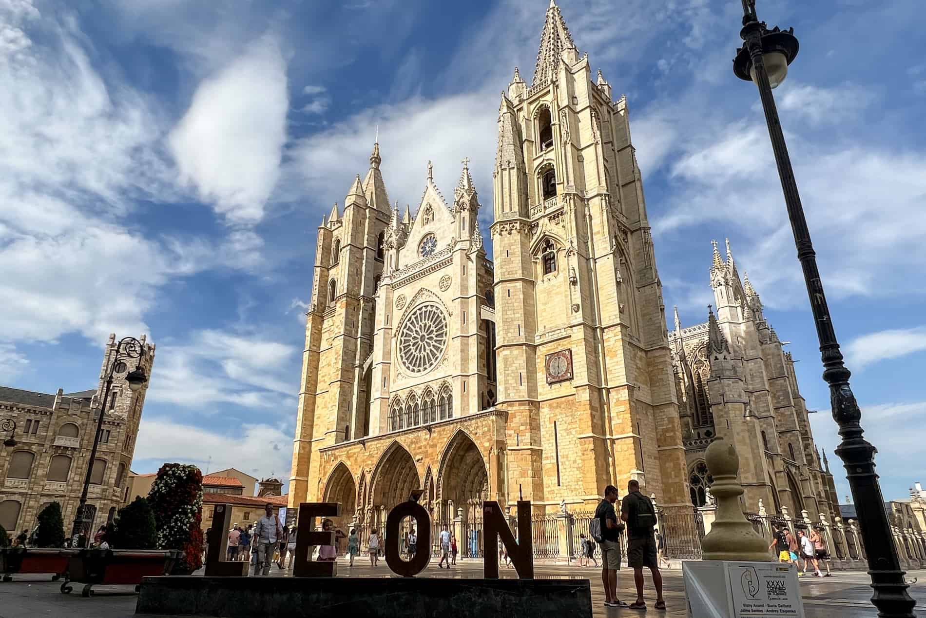 The towering golden gothic structure of Leon Cathedral with a Leon city sign in front of it. 