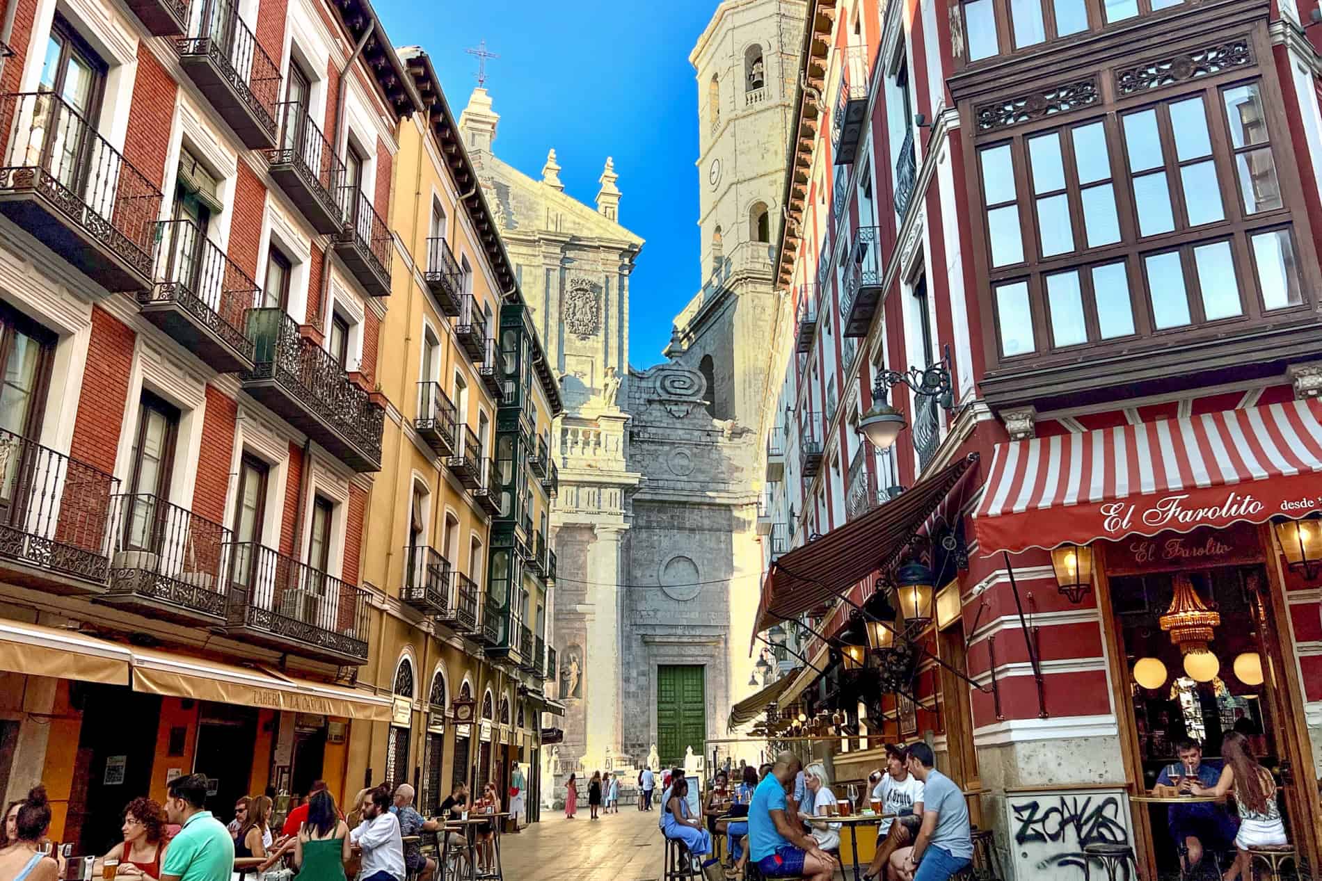 People sitting outside bars on a busy street in front of a cathedral - a street scene from Valladolid, Spain.. 