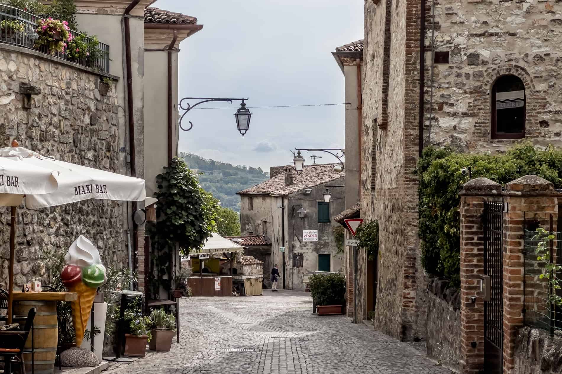 A giant ice cream sculpture and seating area on a village street with silver stone walls and houses in Arquà Petrarca. 