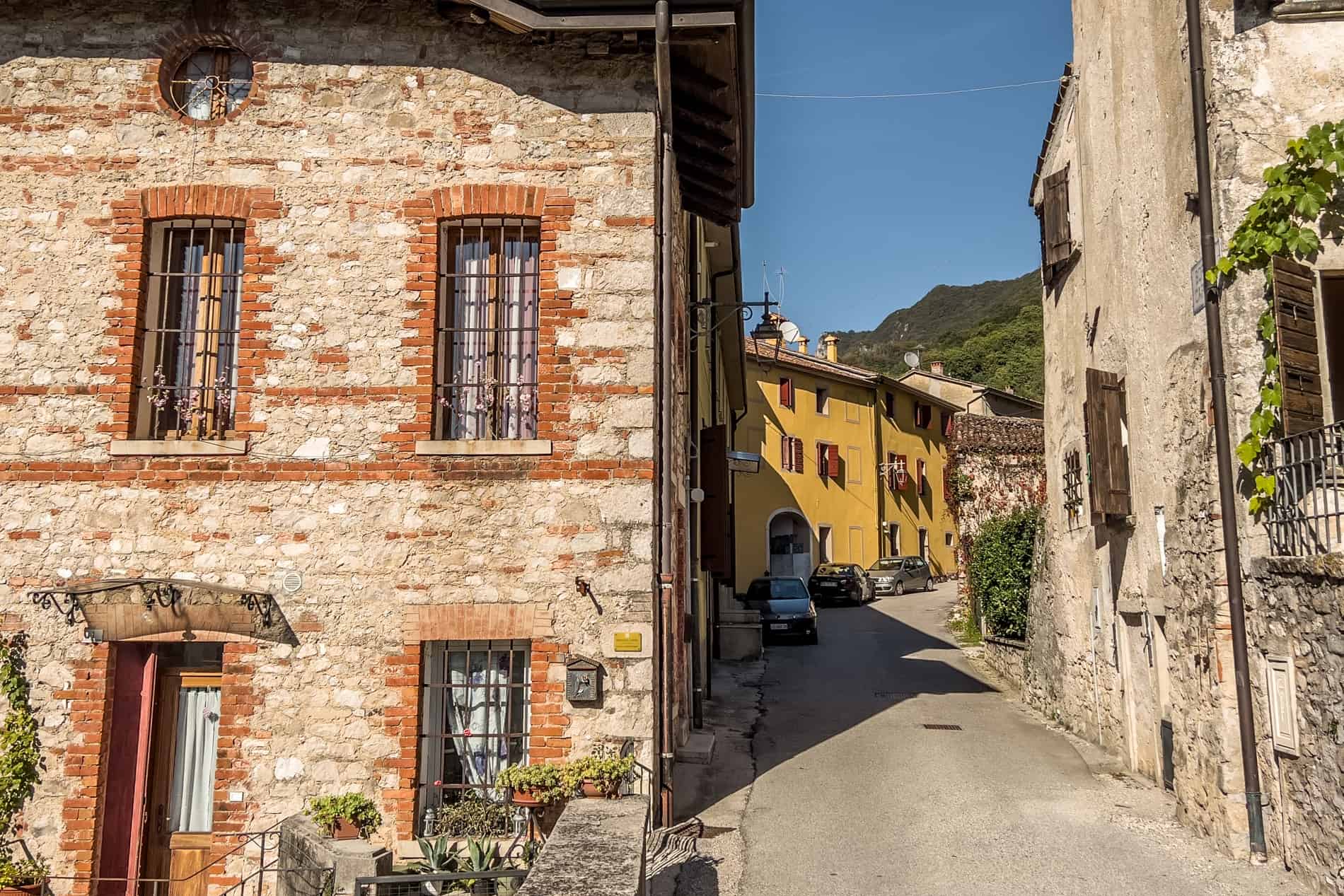 A golden stone house at the start of a street leading to a yellow painted house in Cison di Valmarino village. 