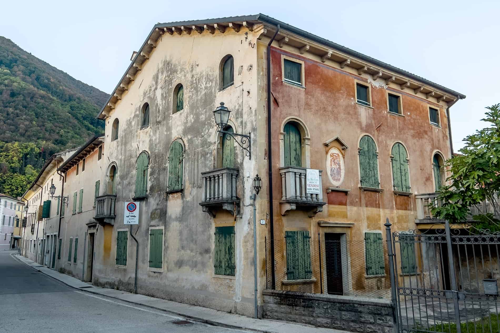 Aged structures with faded orange and yellow paint and green shutters in the village of Follina, Italy. 