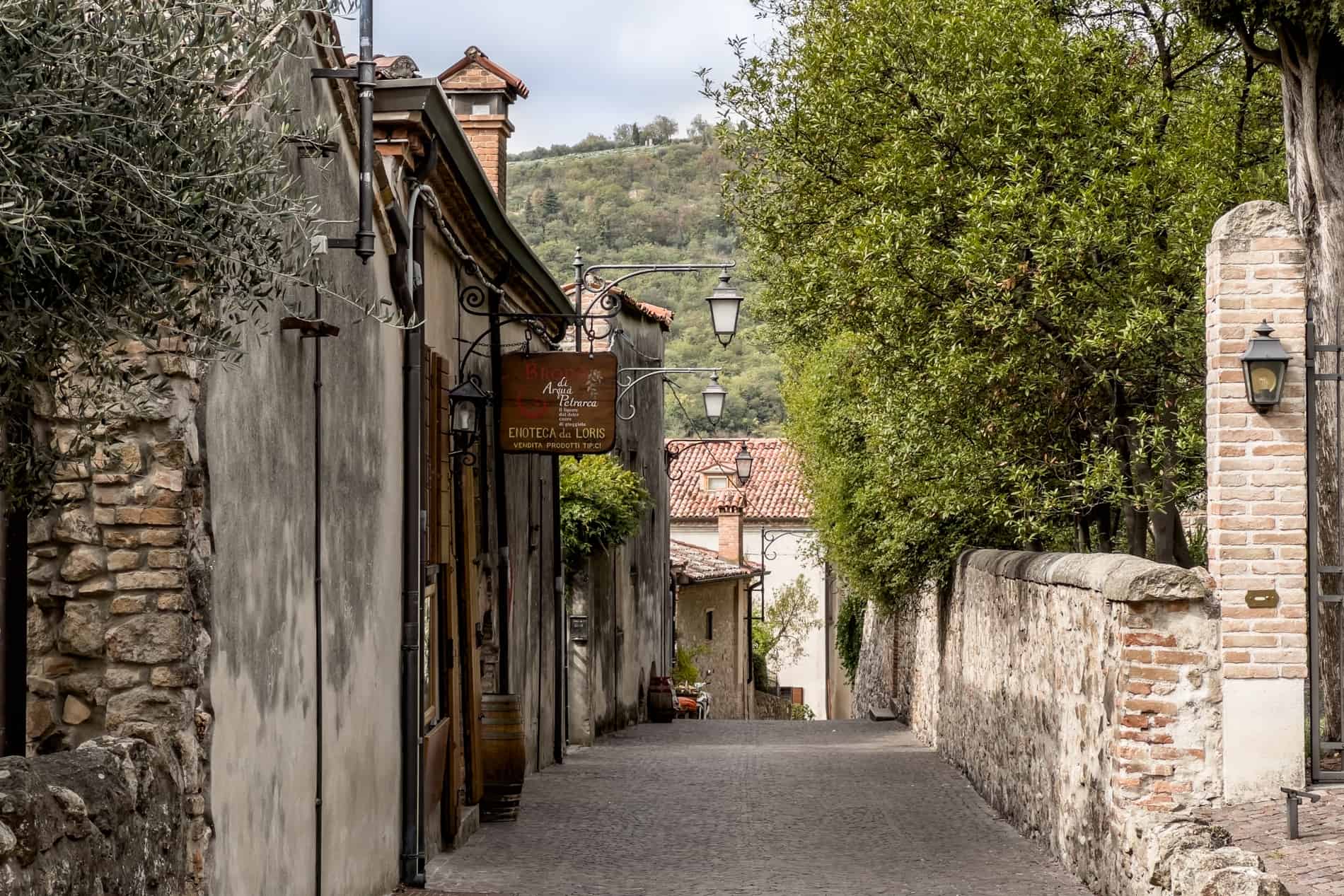 A stone pathway lined with old stone houses, shop signs and lanterns. 