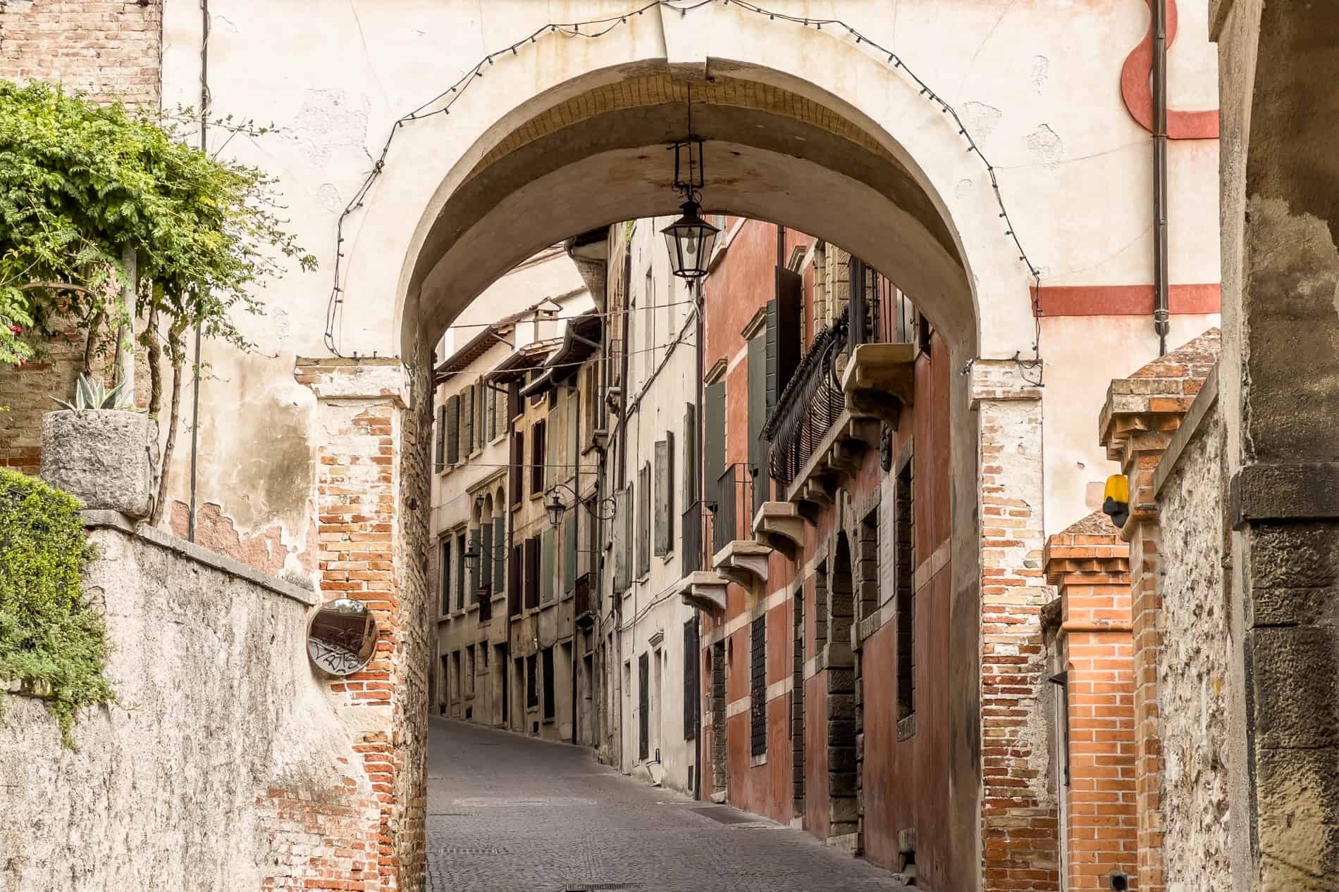 An archway leading to a street of green shuttered houses painted in earthy hues.