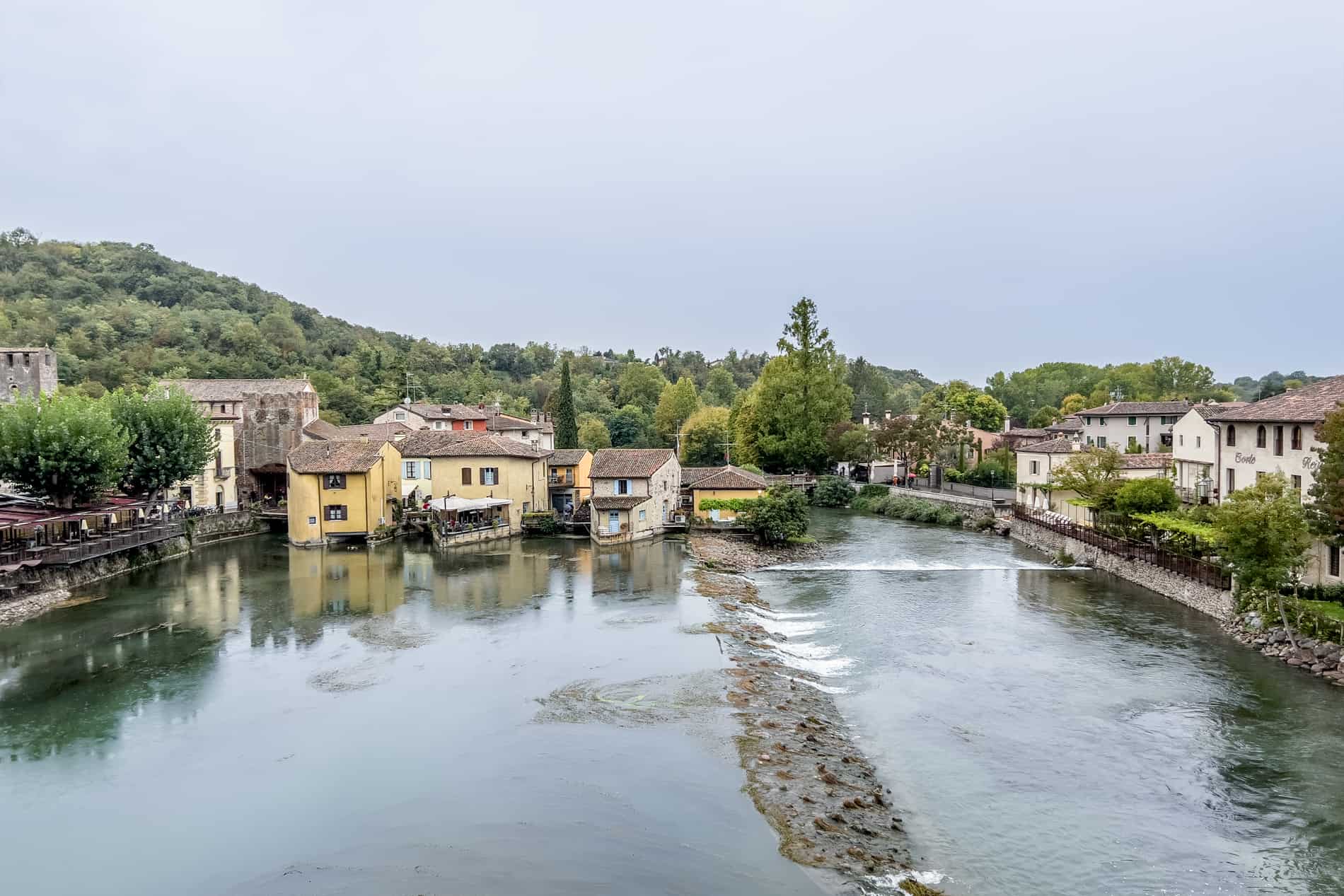 Red brick villages houses lined across a river and backed by green hills.