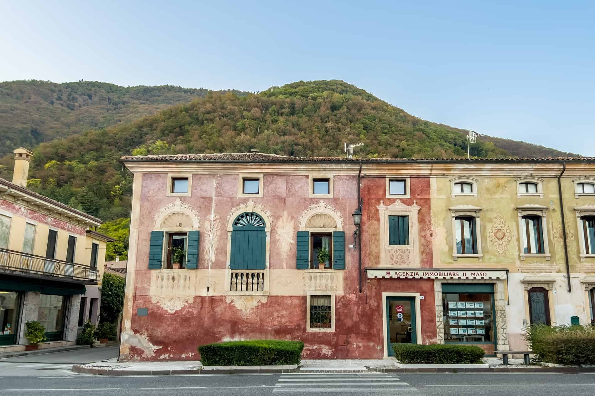 Red and yellow painted houses with window design features and wooden shutters in a village set within the hills. 