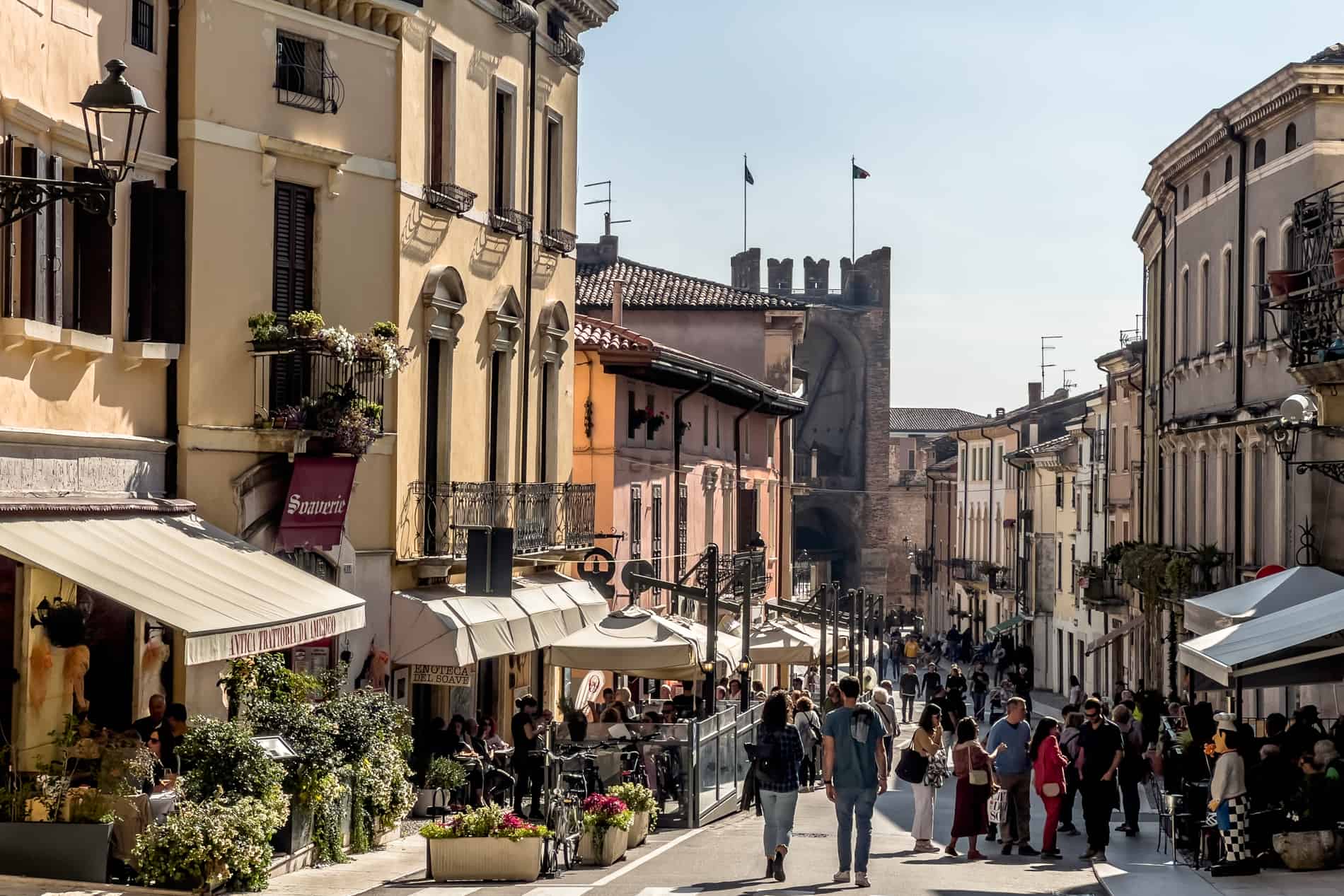 Pastel coloured buildings line a street that leads to a fortress gate in Italy's most beautiful village, Soave. 