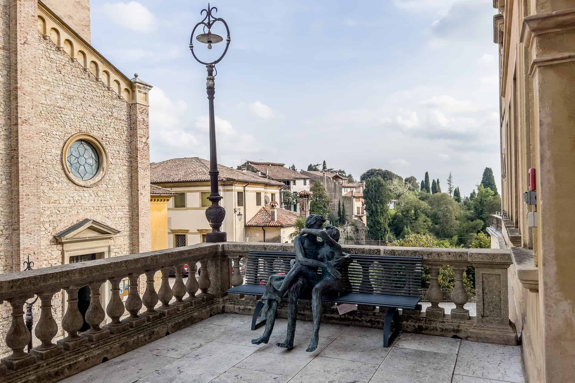 A metal sculpture of a kissing couple sitting on a bench, in the village of Asolo, Italy. 