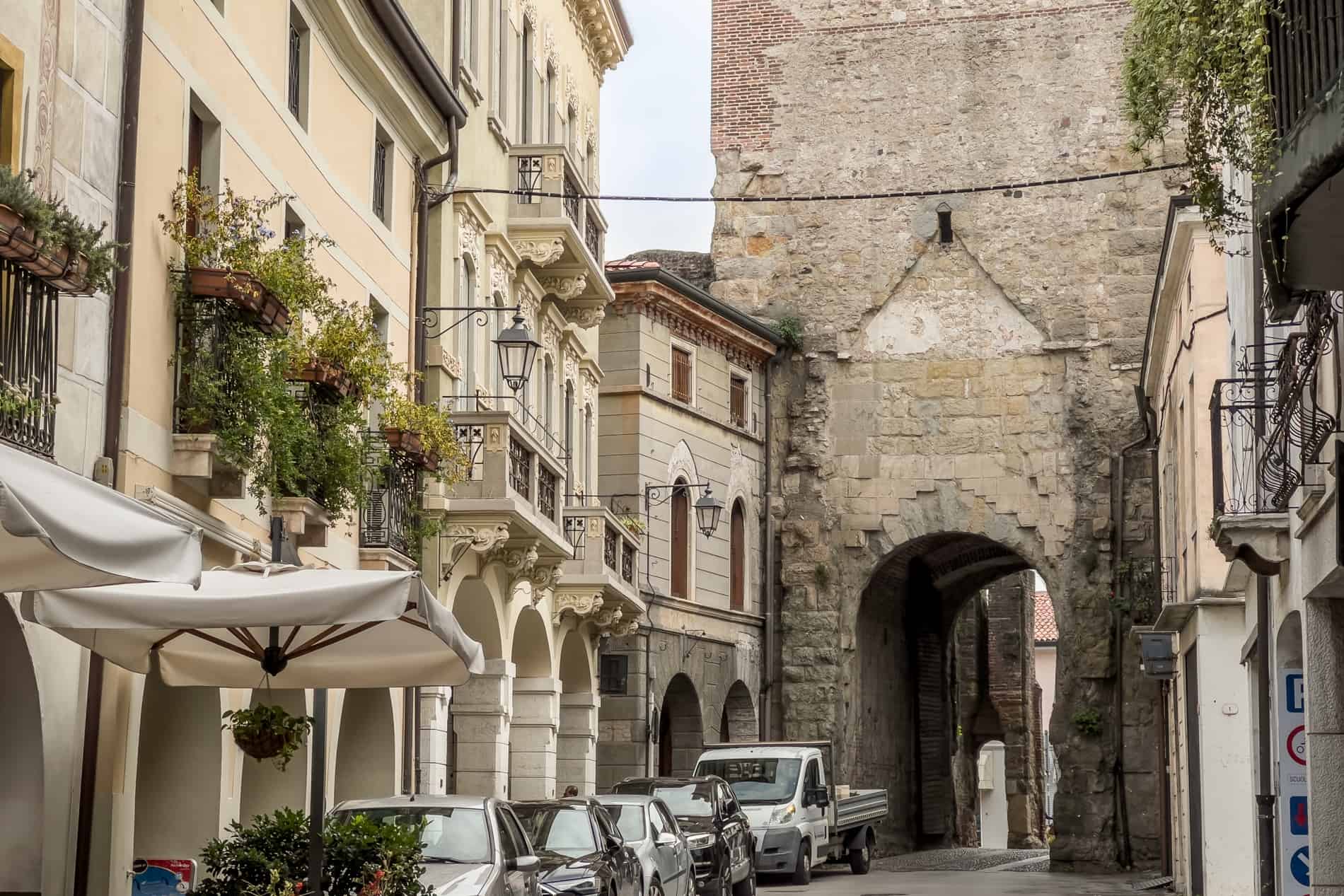 Creamy coloured buildings with cars outside, line a road with a stone tower at the end. 