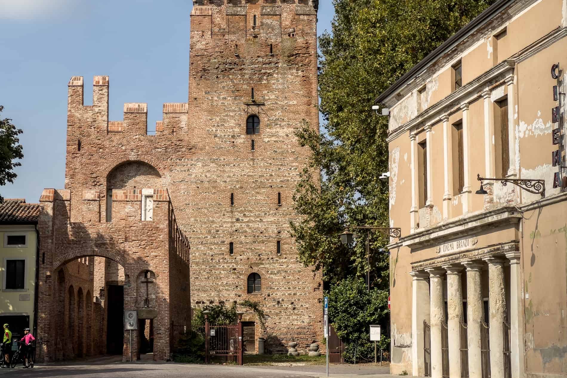 A medieval fortress tower stands next to a timeworn columned, theatre structure. 