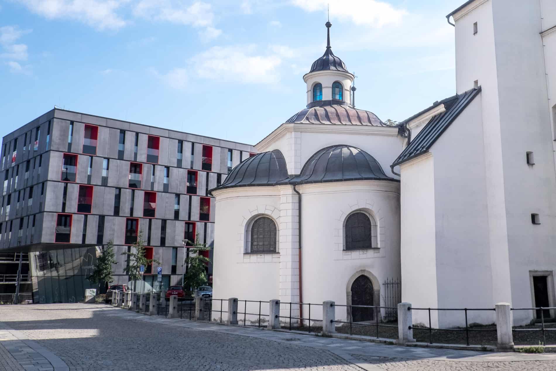 A 13th-century white church next to a modern grey office block. 