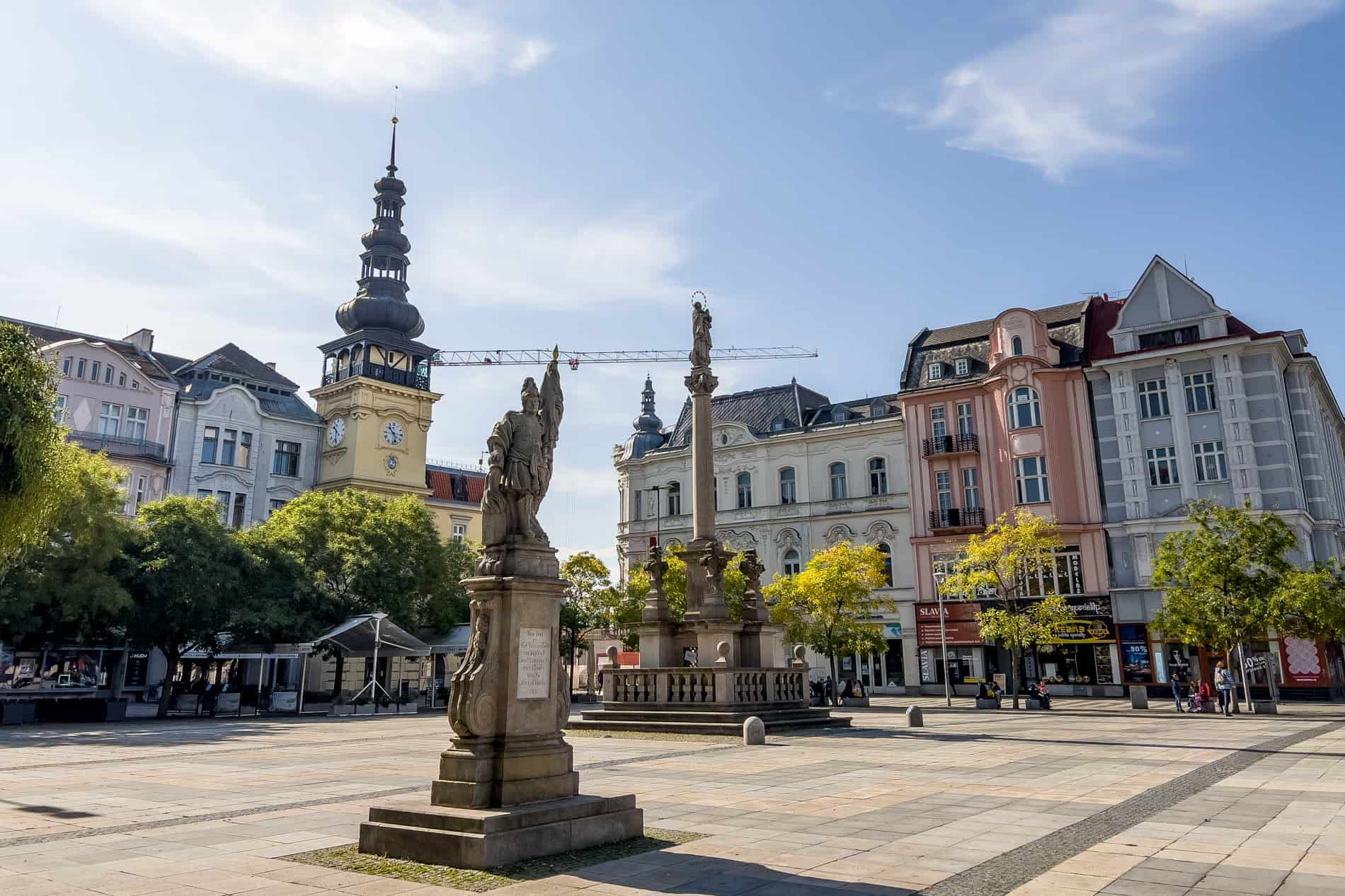 A statue and a column in a city square surrounded by buildings in pastel colours. 