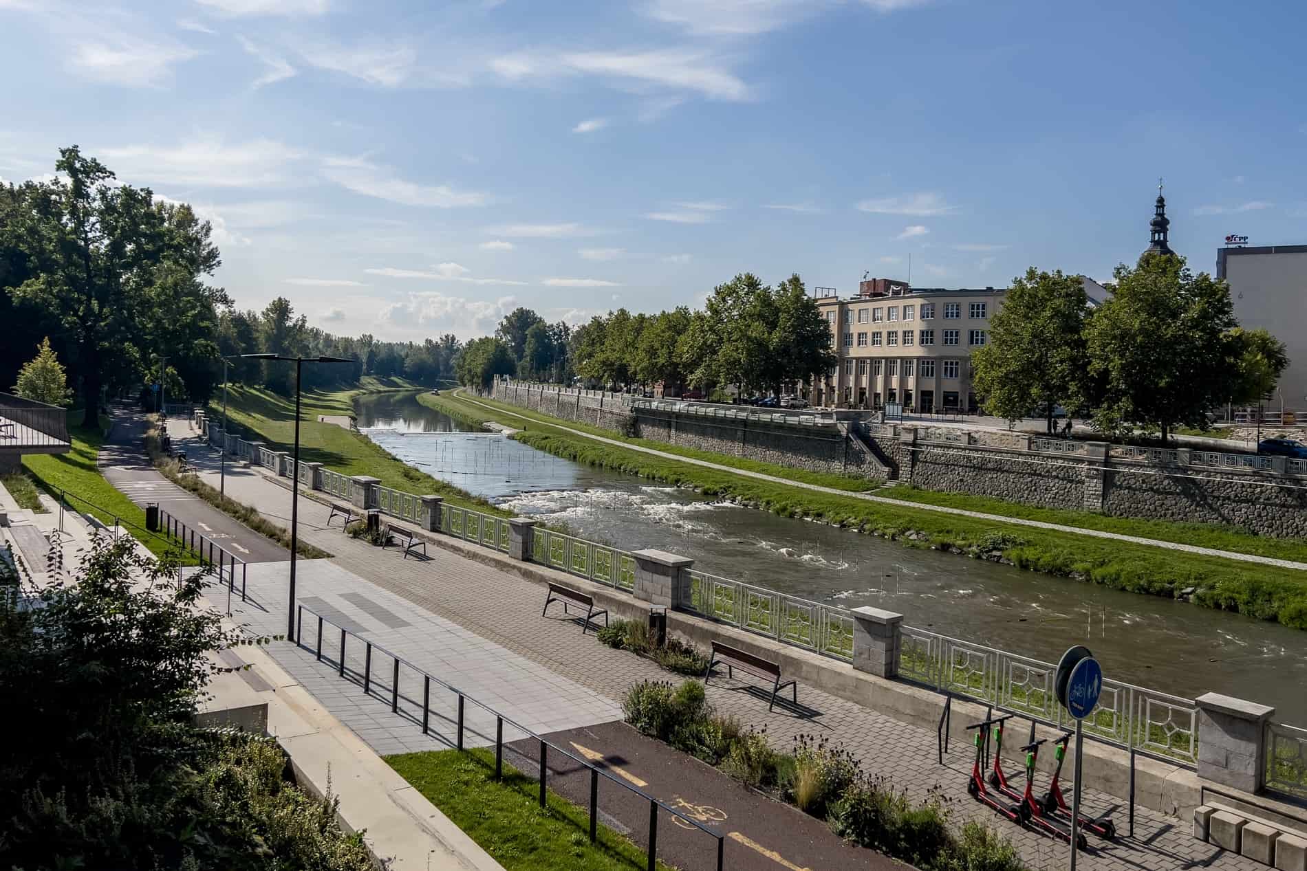 A view of a stretch of the Ostravice River in Ostrava with green banks and walking paths. 