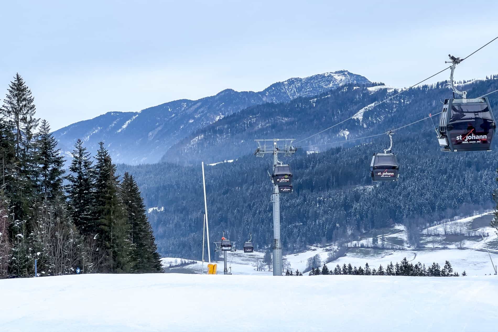 Cable cars with St. Johann in Tirol branding going up the snow-covered mountain. 