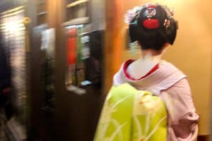 The back of a Geisha in the Gion district of Kyoto, Japan, wearing a pink robe with a green sash.