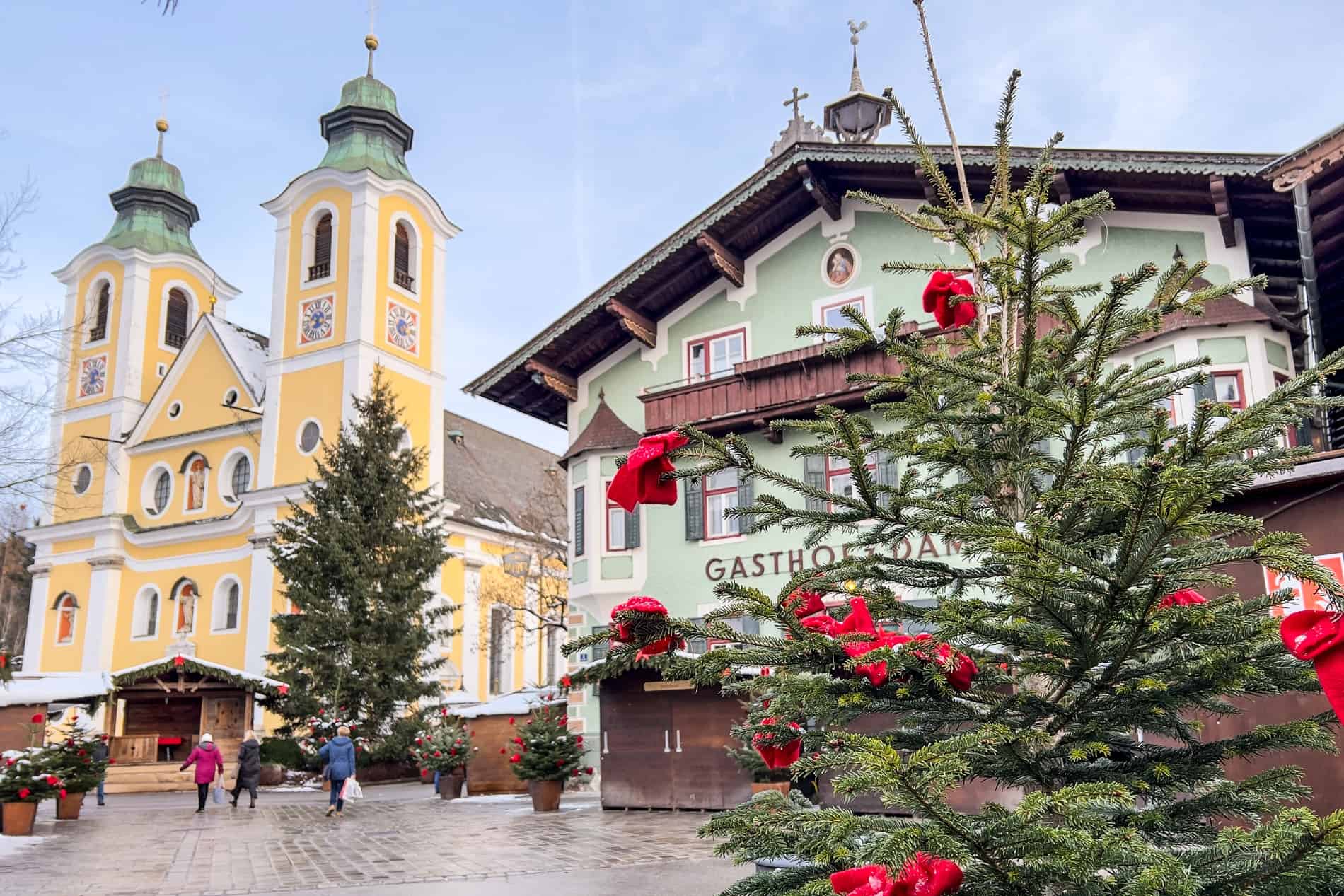 The yellow church and mint green guest house in the main square of St. Johann in Tirol town at Christmas. 