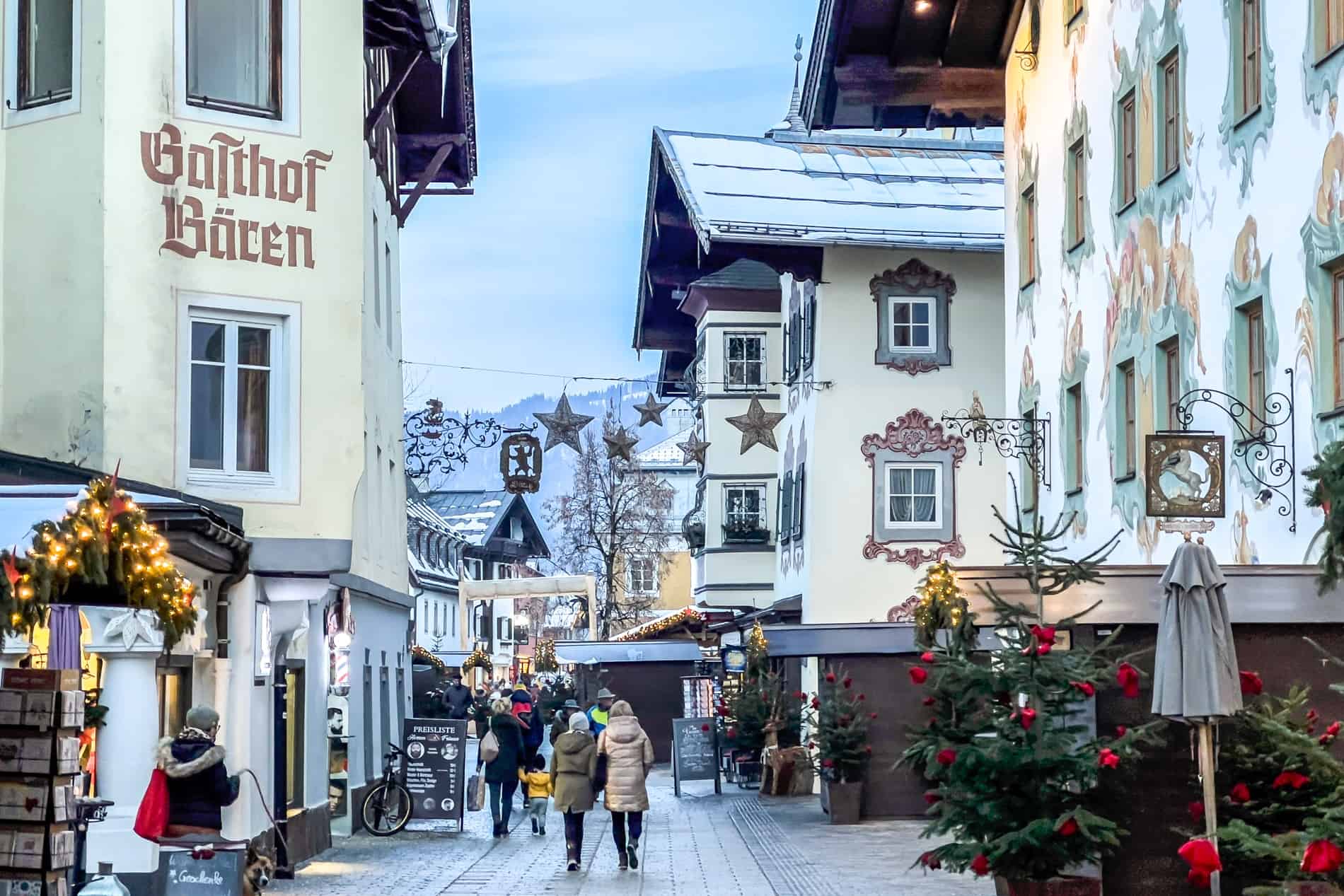 A street in St. Johann in Tirol with painted buildings, filled with Christmas decorations and wooden market booths. 