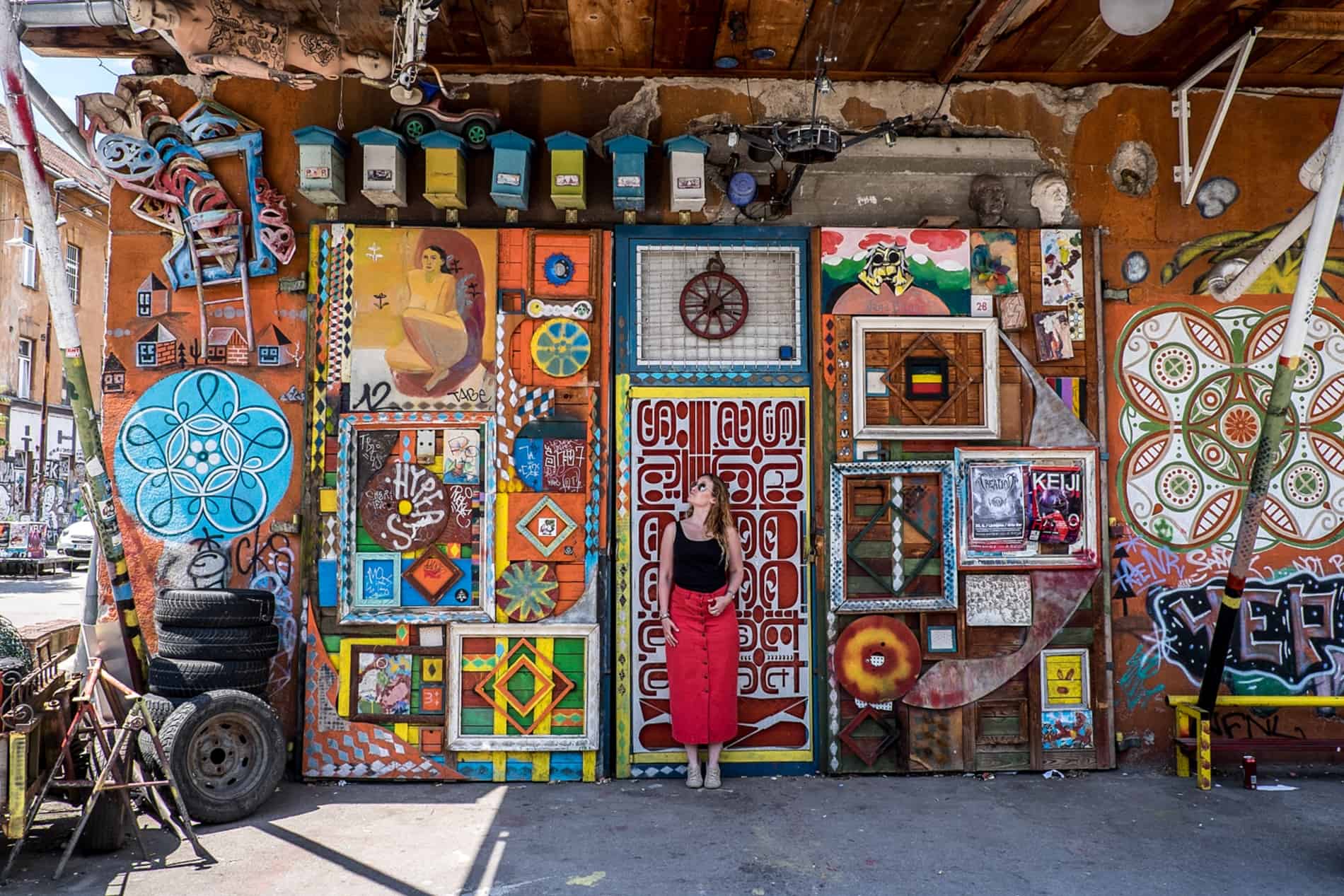 A woman in a red skirt stands in front of a decorated wall at one of the many art studios in Metelkova in Ljubljana.