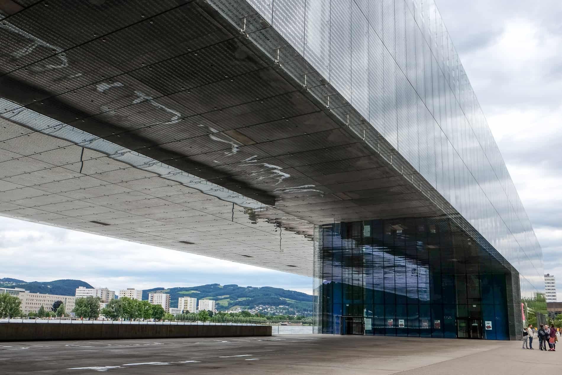 A long, reflective glass art museum building in Linz next to the Danube river. 
