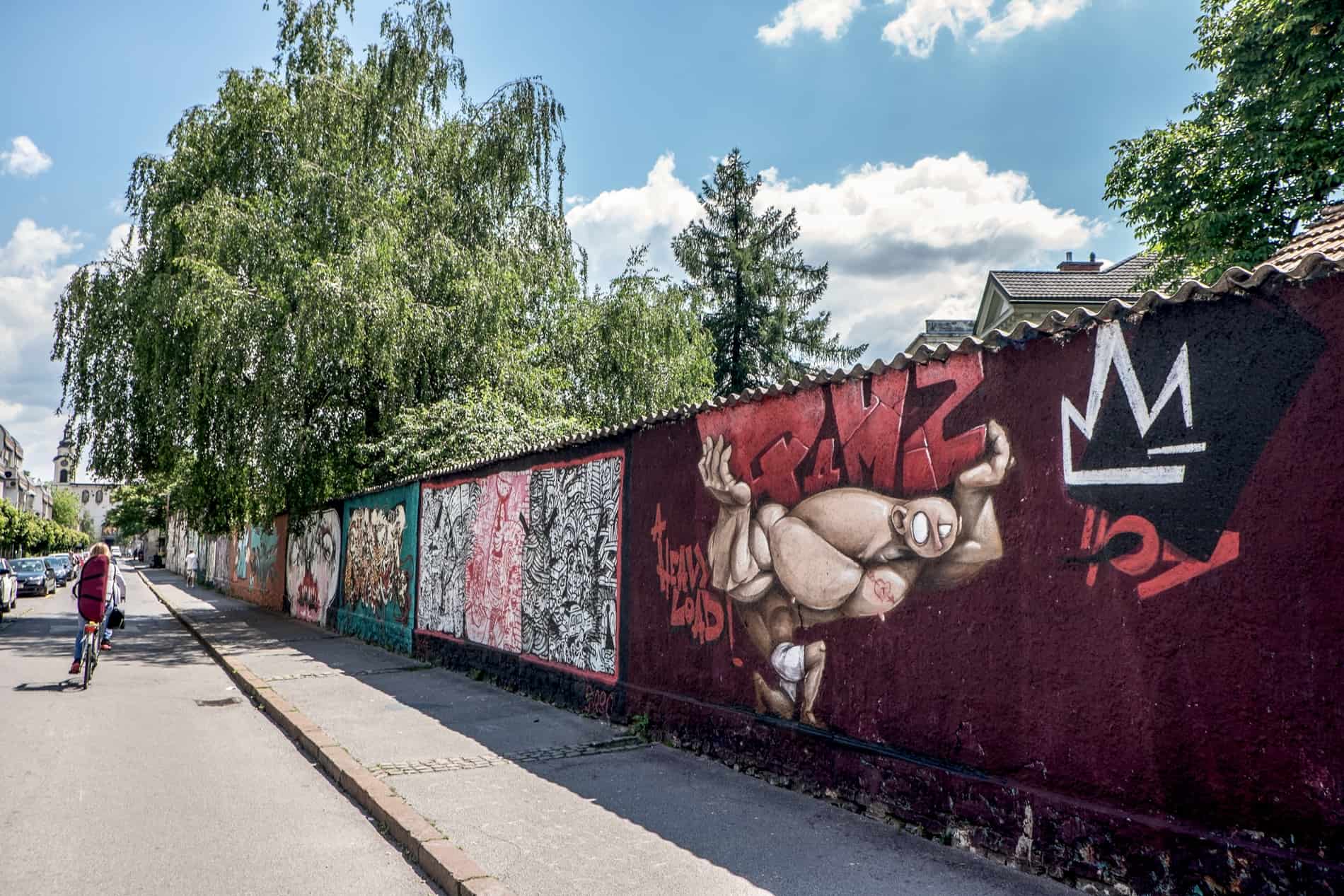 A cyclist rides past a wall covered in art murals, marking the entrance to the creative Rog Factory in Ljubljana. 