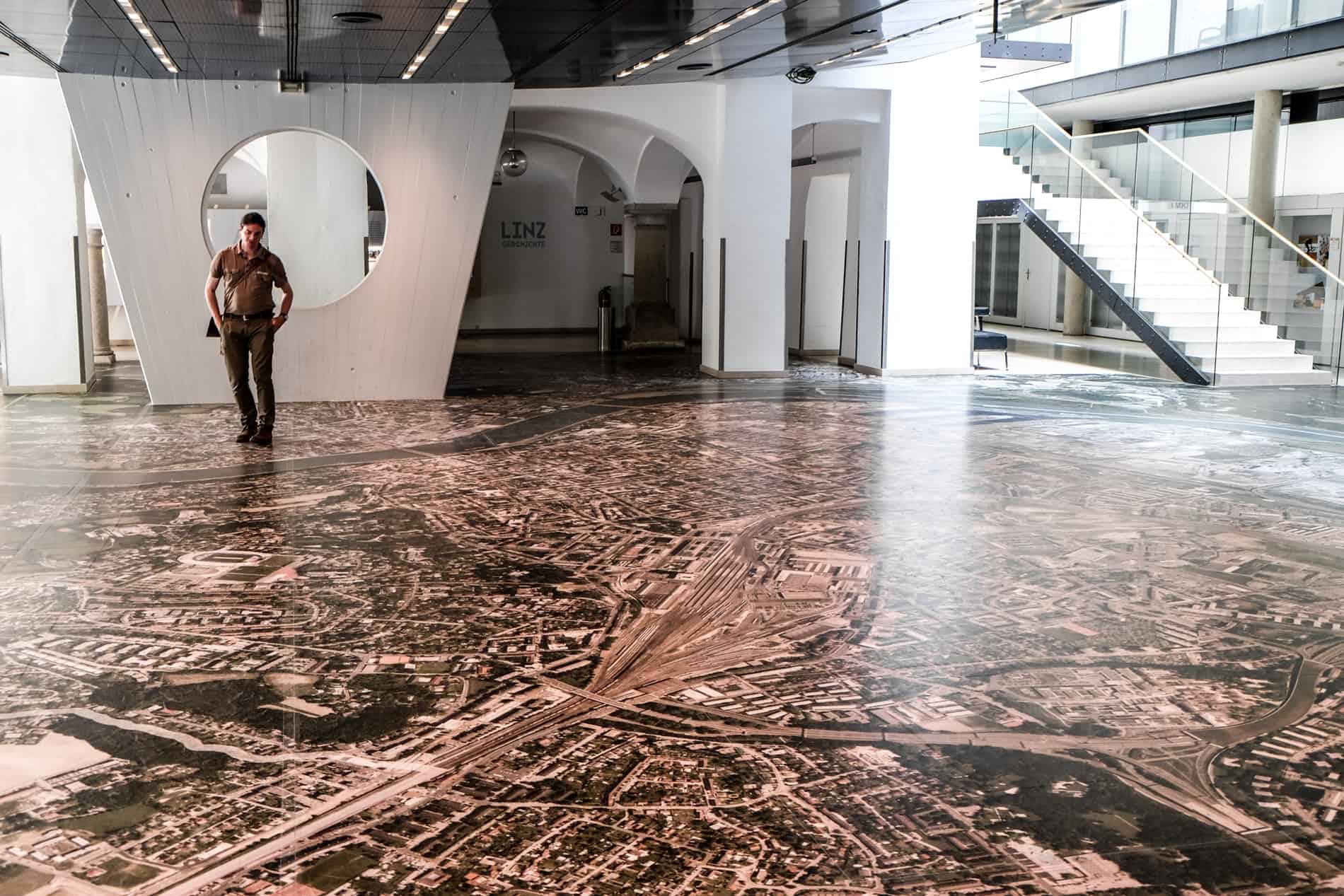 A man stands on a giant aerial city view of Linz on the floor of the city's Town Hall. 