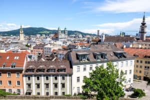 Elevated view over the city of Linz in Austria, with pastel buildings and church spires, backed by hills.