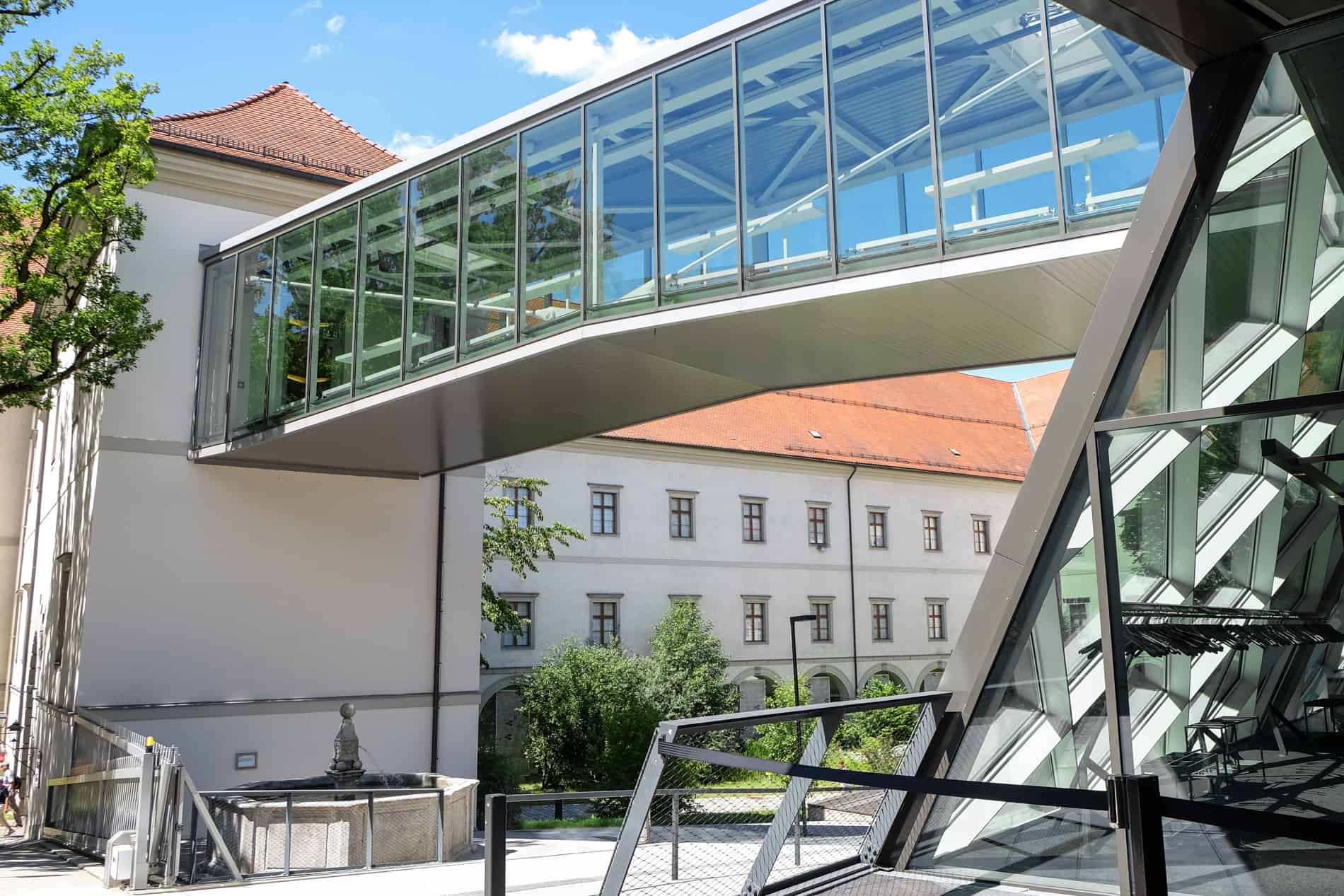 A glass tunnel leading to an old white building - the modern construction of the South Wing of Linz Castle.