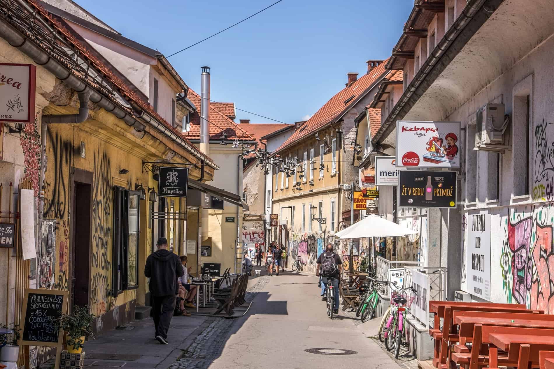A narrow, gritty street in Ljubljana full of graffiti, street art murals, and unkempt buildings. 