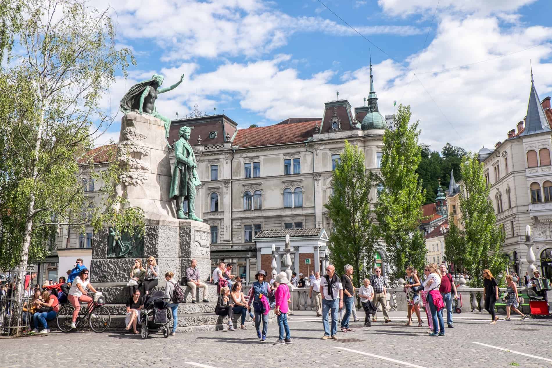 Mint green statues, a square full of people and the white washed buildings of Ljubljana Old Town.
