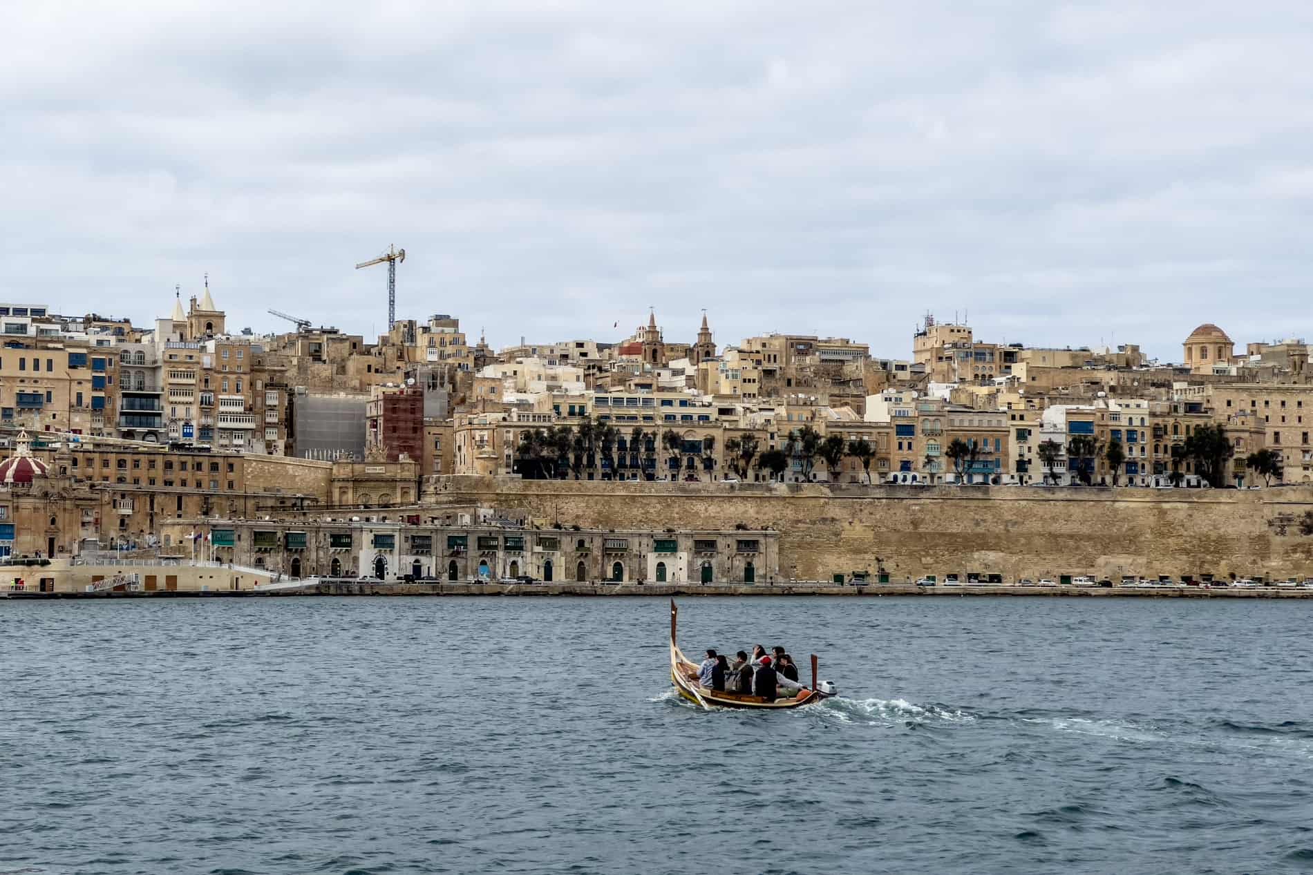People on a wooden water taxi boat in Malta cruising on the water in the direction of the walled city of Valletta. 