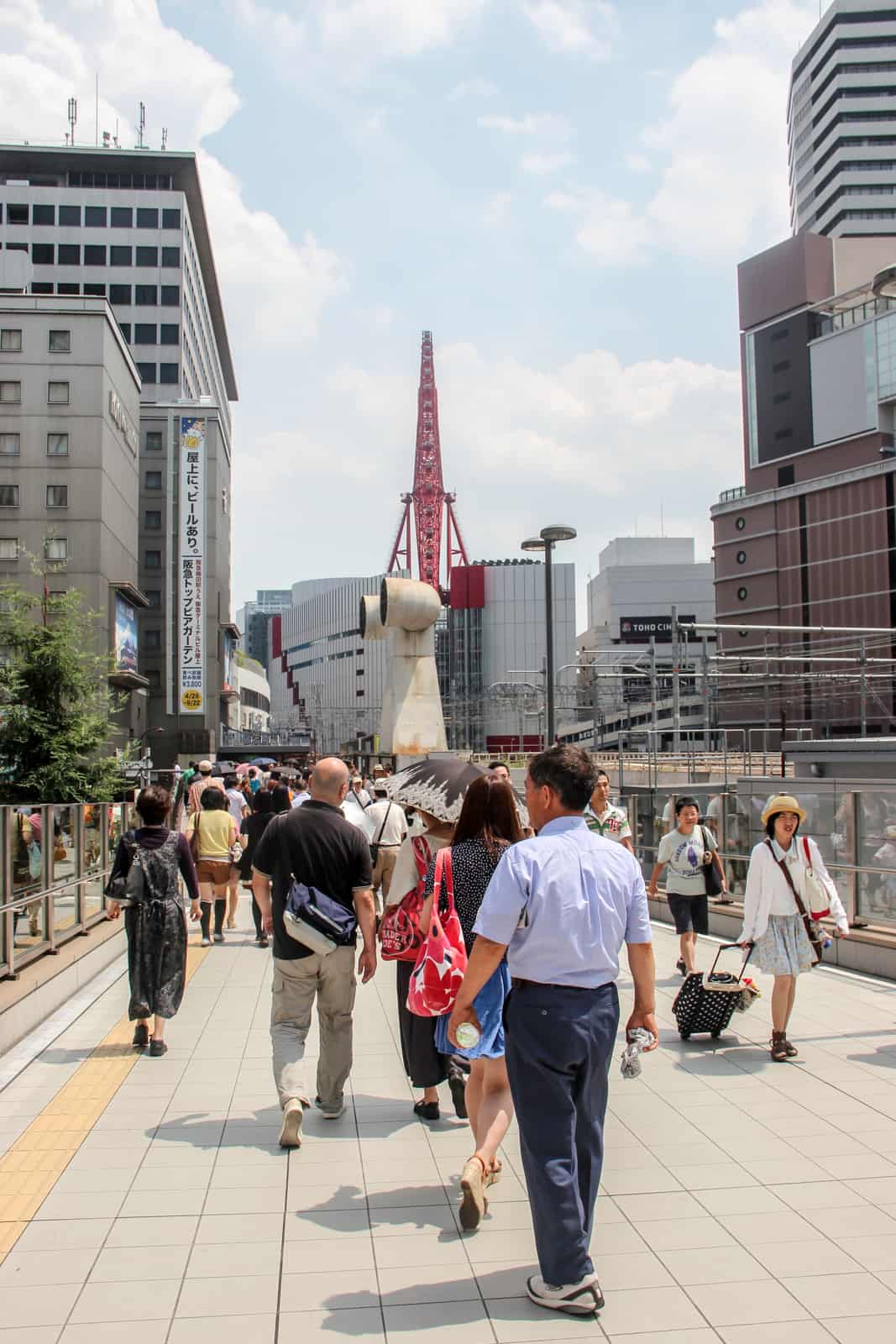 People walking towards a shopping centre in Osaka with a red ferris wheel on top of it. 