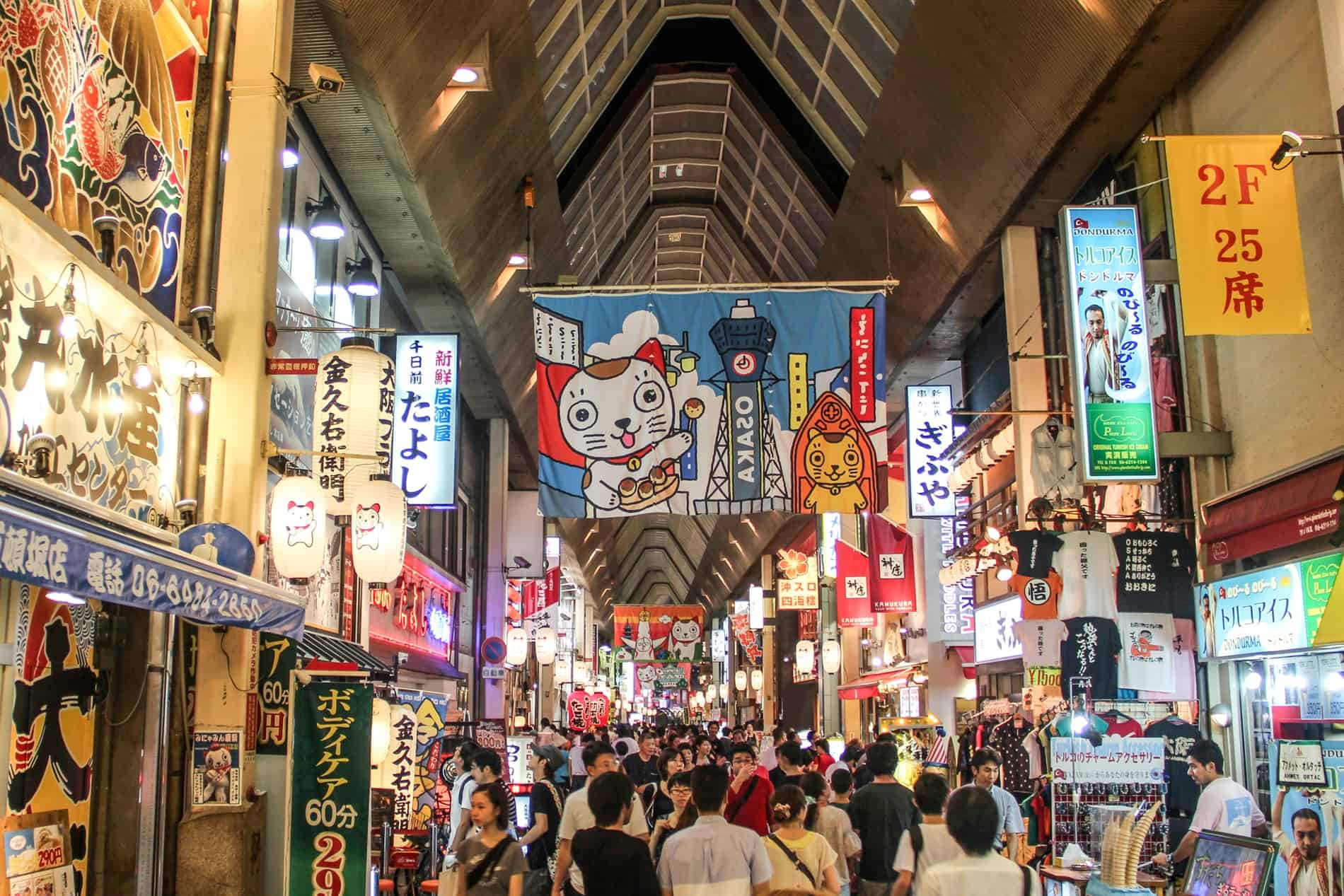 People fill a bright and colourful shopping arcade on Dotonburi Street, Osaka, lined with cartoon posters and lit-up signs. 