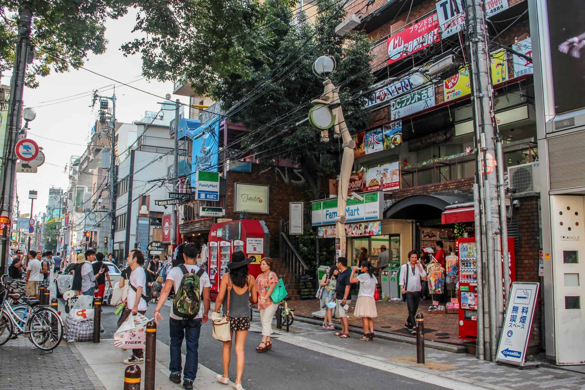 People fill a bust street lined with stick men figure street lights, multi-level shops, and bars in Osaka's American Village. 