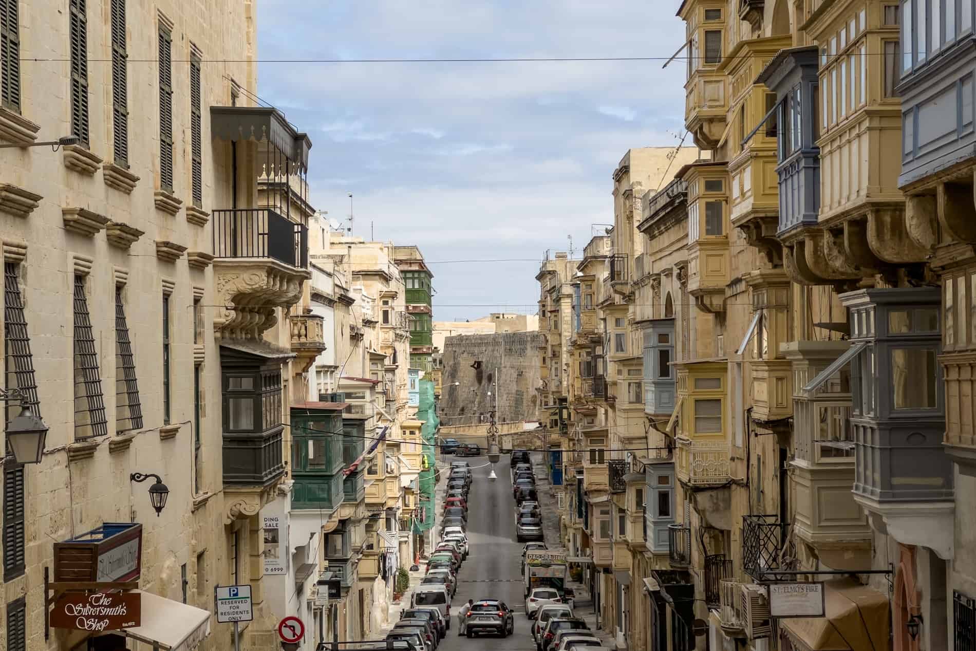 Honey limestone buildings with balconies lining a long and sloping street in Valletta, Malta. 