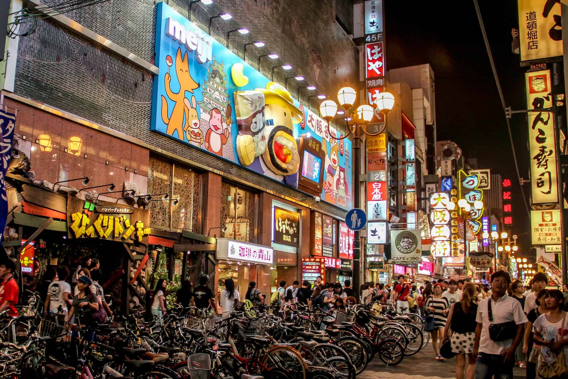 A huge crowd of people fill the quirky decorated streets of Osaka's Dotonburi district, filled with bright lights, large images and building sculptures. 