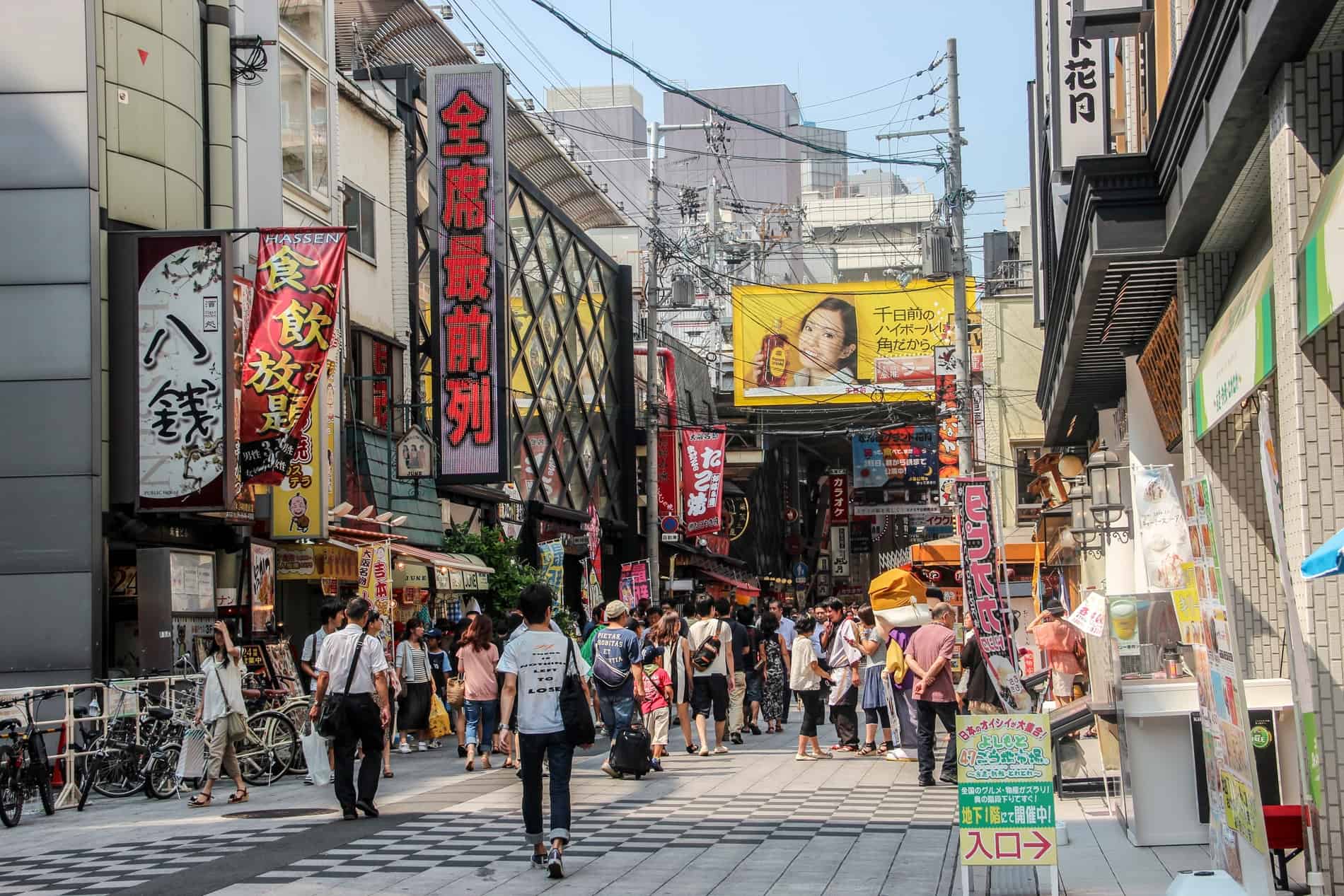 A crowded street in Osaka lined with stores and advertising signs, leading into a long shopping arcade. 