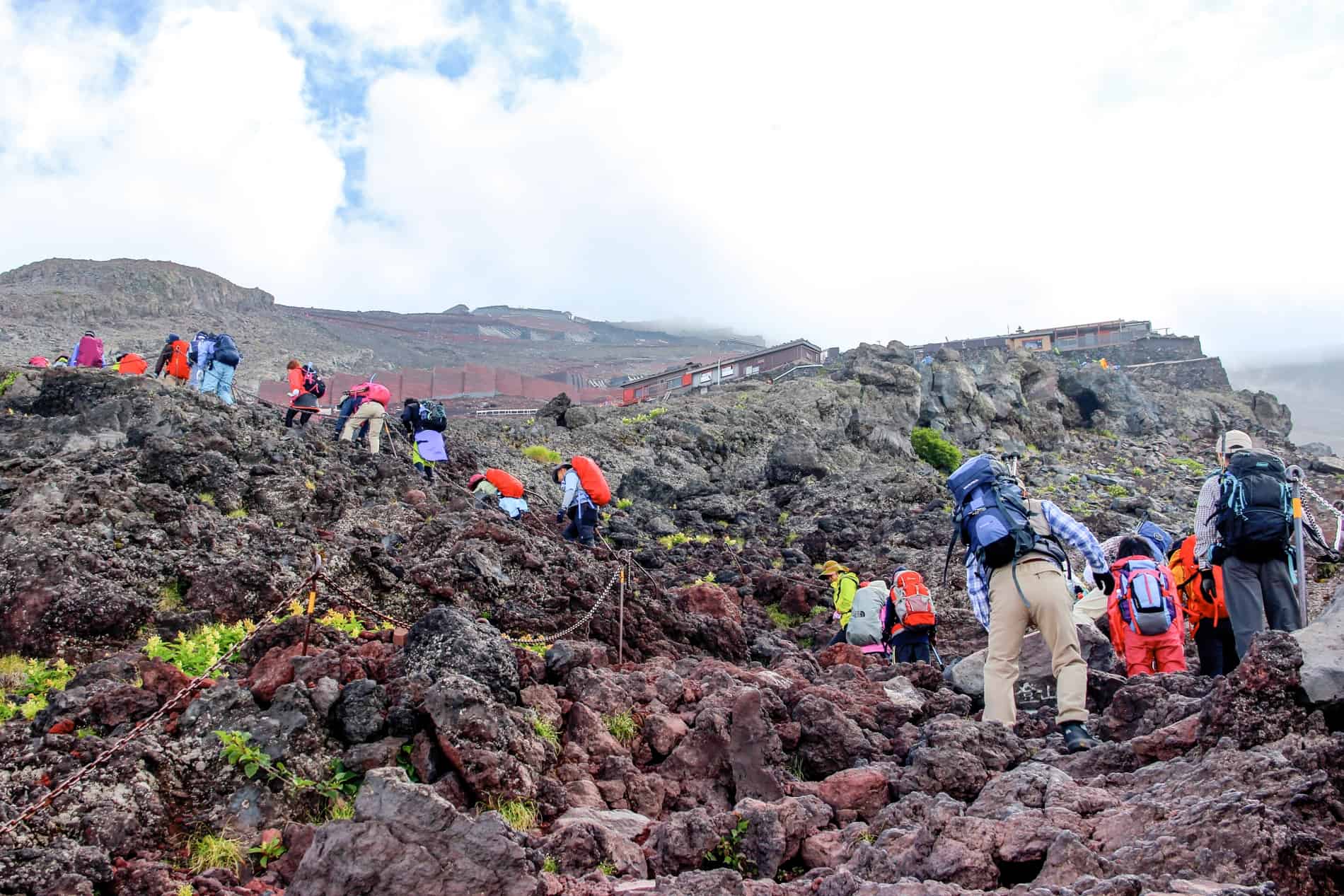 Hikers in colours clothing and trekking gear walking up the dense rocky paths on Mt Fuji in Japan.
