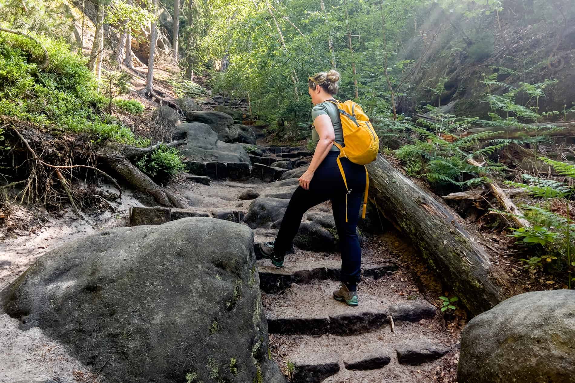 A woman hiking up steep rock stairs at the start of the Jetřichovice Loop hike in Bohemian Switzerland. 