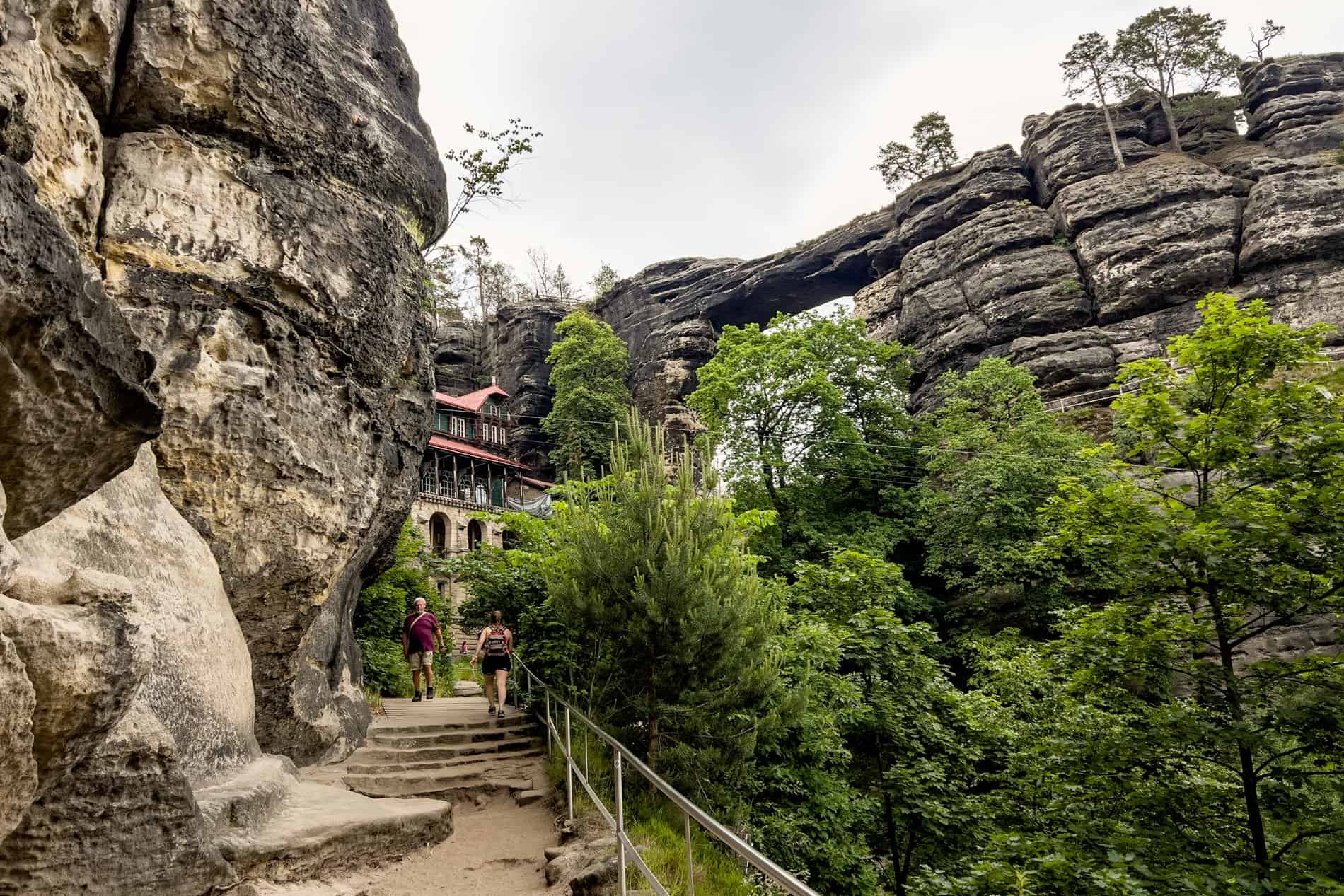 Visitors on the hiking pathway in front of the Sokolí hnízdo (Falcon's Nest) chateau and the stone archway Pravcicka Gate. 