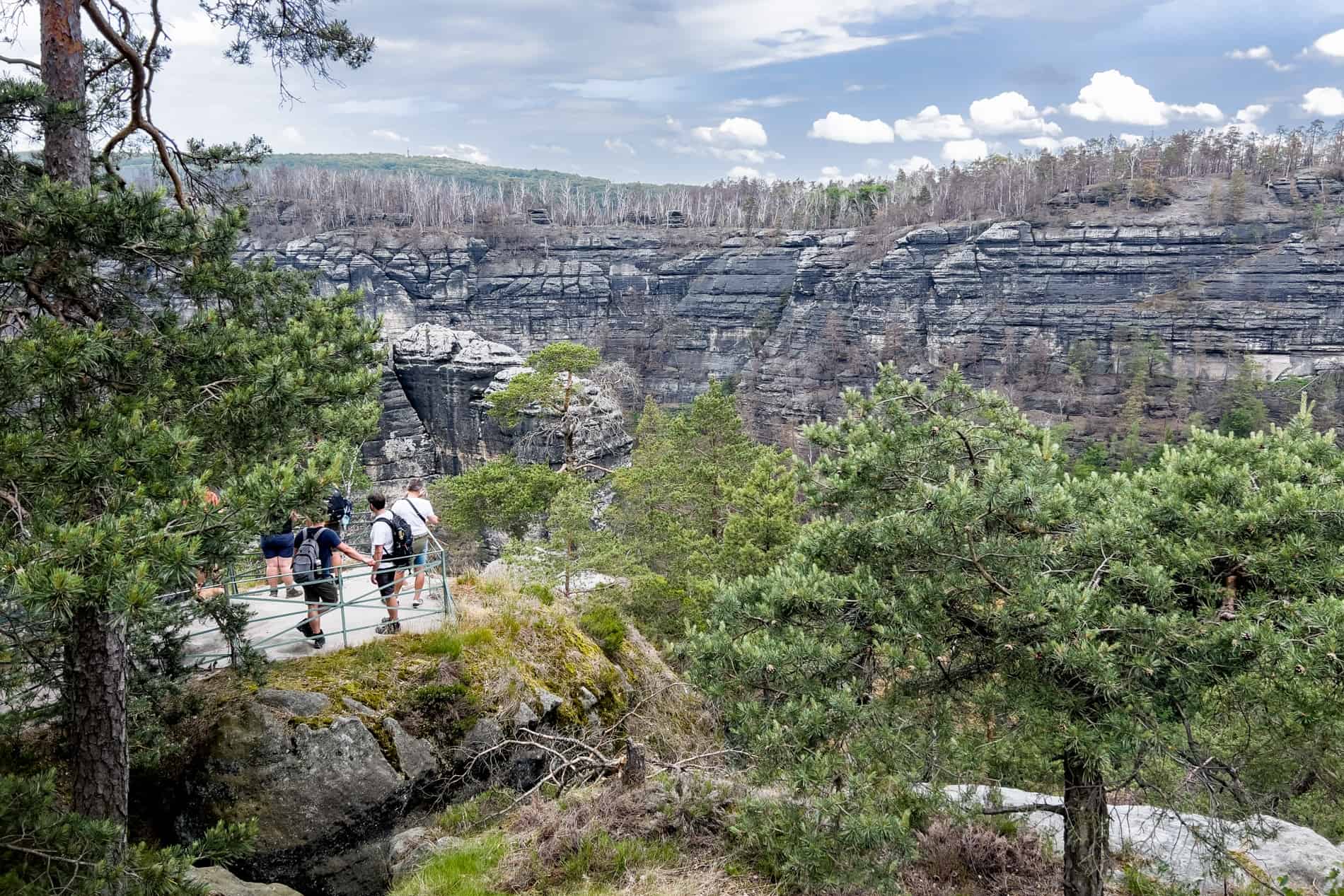 Visitors at a viewing platform in front of a sandstone rock wall formation in Bohemian Switzerland National Park. 