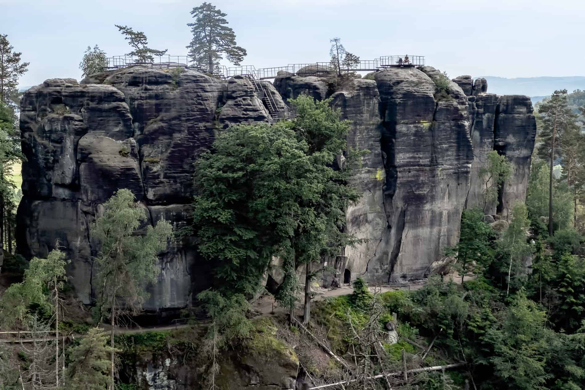 People sit at the top of the tall, colossal rock face of Saunstejn Rock Castle (Pod Šaunštejnem) in the Bohemian Switzerland forest. 