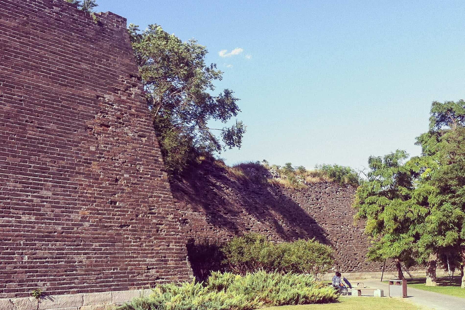 People sitting on a bench on a paved park next to an ancient fortification wall in Beijing. 