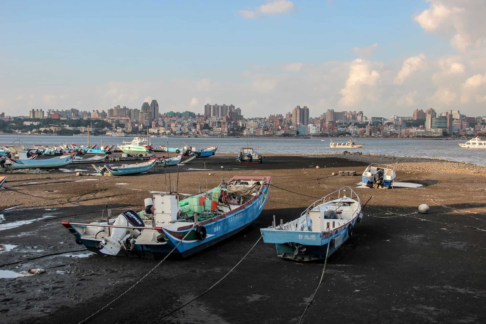 Boats on a shoreline facing the direction of a built up city on the other side of the river. 