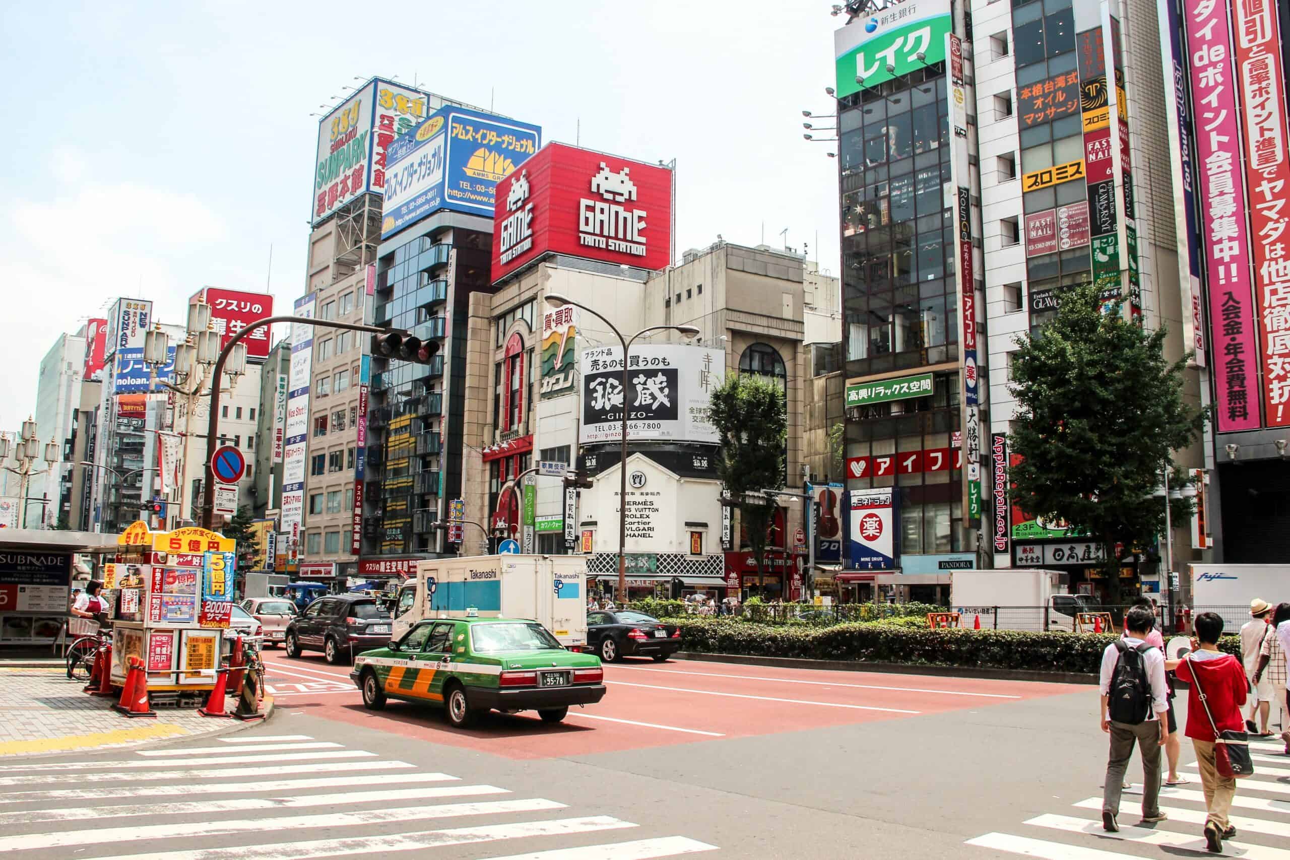 A taxi drives down a wide road in Tokyo, with modern high rise and glass buildings either side.