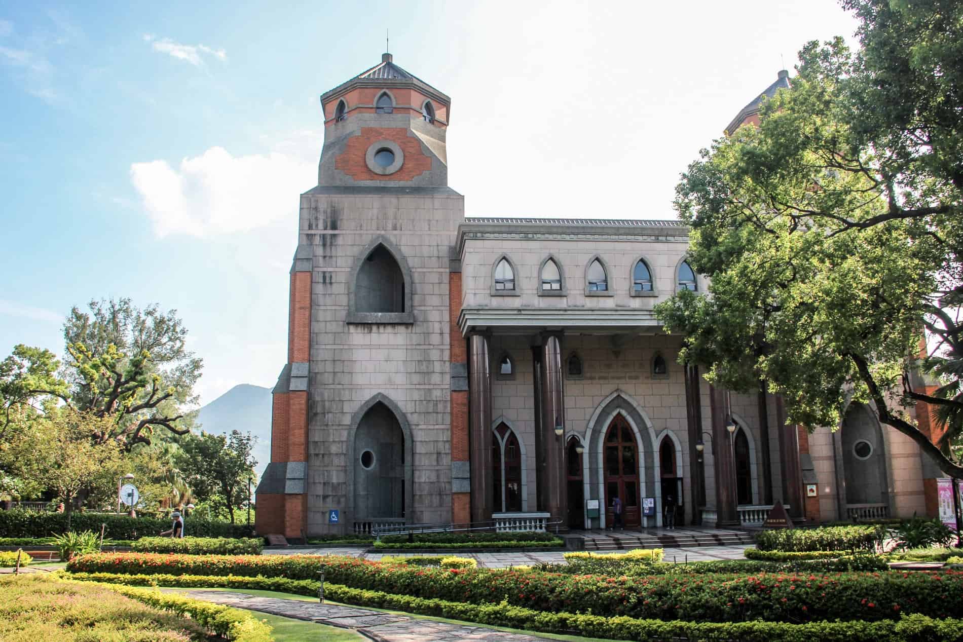 A redbrick and white stone Grand Chapel of Aletheia University in a garden setting. 